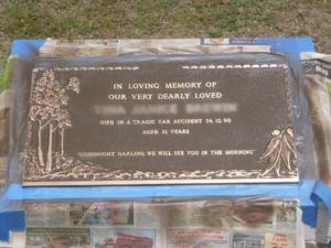 Bronze memorial plaque with engraved text and decorative trees, set on newspaper with blue painter's tape.