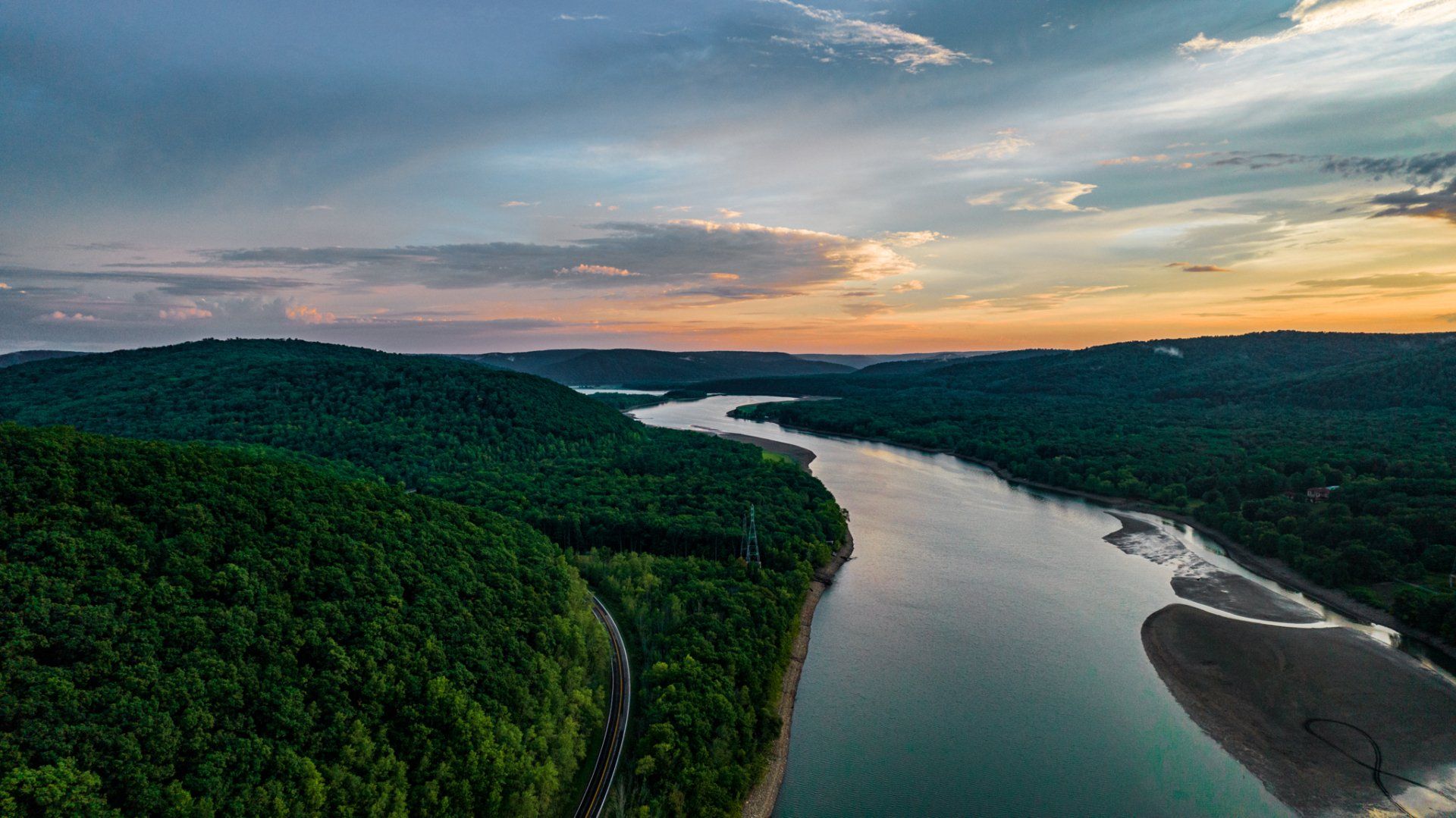 An aerial view of a river surrounded by trees and mountains at sunset.