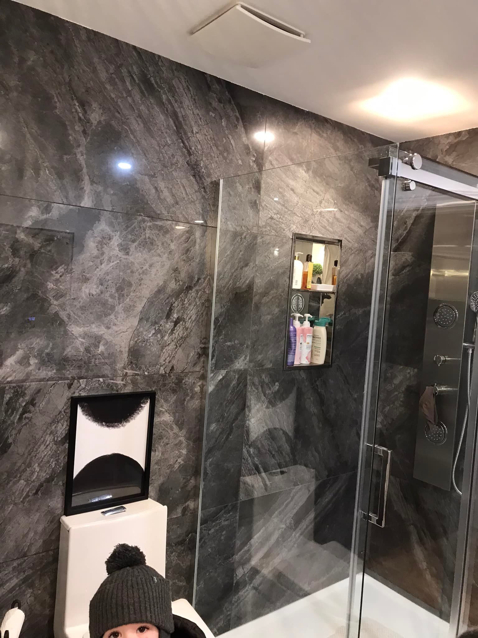 Une salle de bains moderne avec des carreaux muraux foncés texturés imitation pierre, une cabine de douche en verre et une étagère murale.