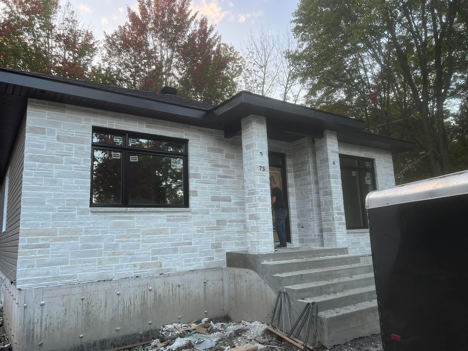 Extérieur d'une maison moderne de plain-pied avec un revêtement en pierre gris clair, des finitions noires et un escalier d'entrée en construction.