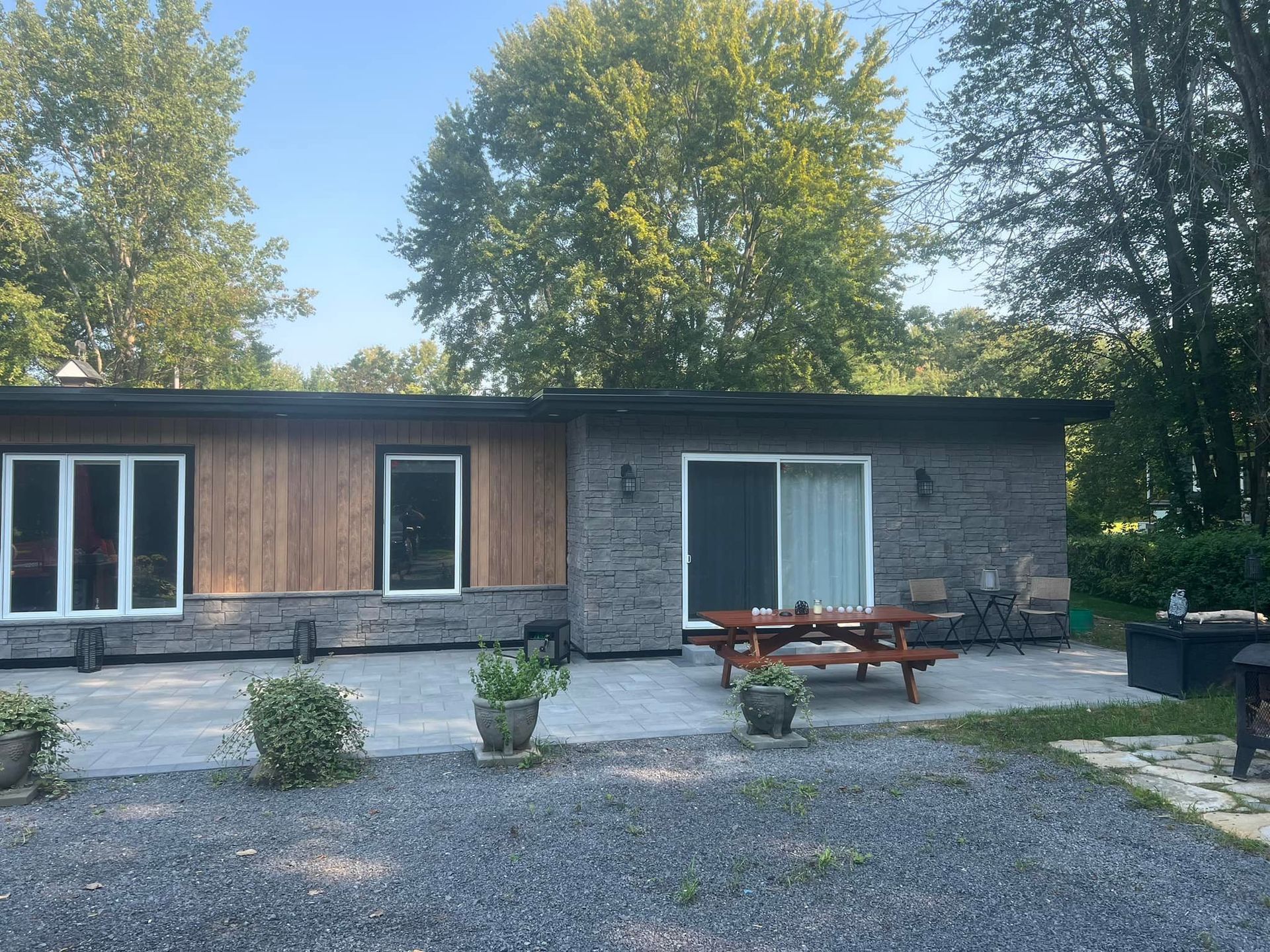 Une maison de plain-pied avec un bardage en bois et des murs en briques de pierre, dotée d'une terrasse avec une table de pique-nique par une journée ensoleillée.