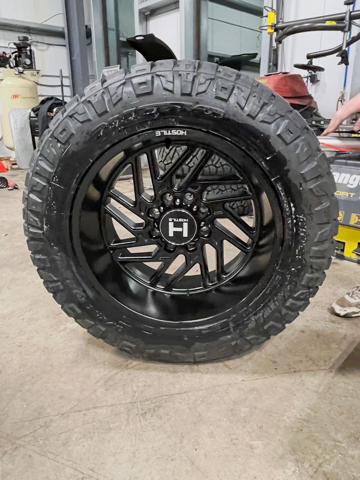 Black off-road tire on a glossy black alloy wheel in a workshop garage