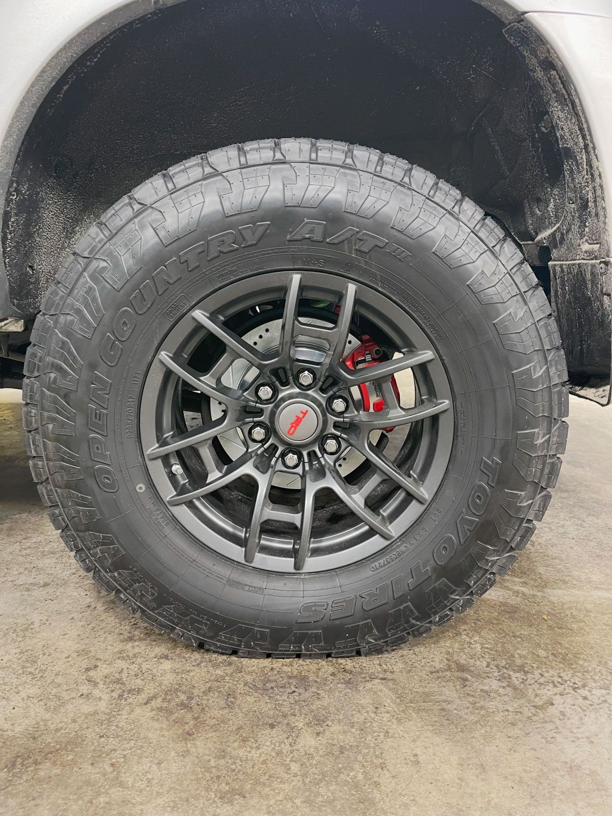 Close-up of a truck wheel with off-road tire, gray rim, and red brake caliper on a wet concrete surface