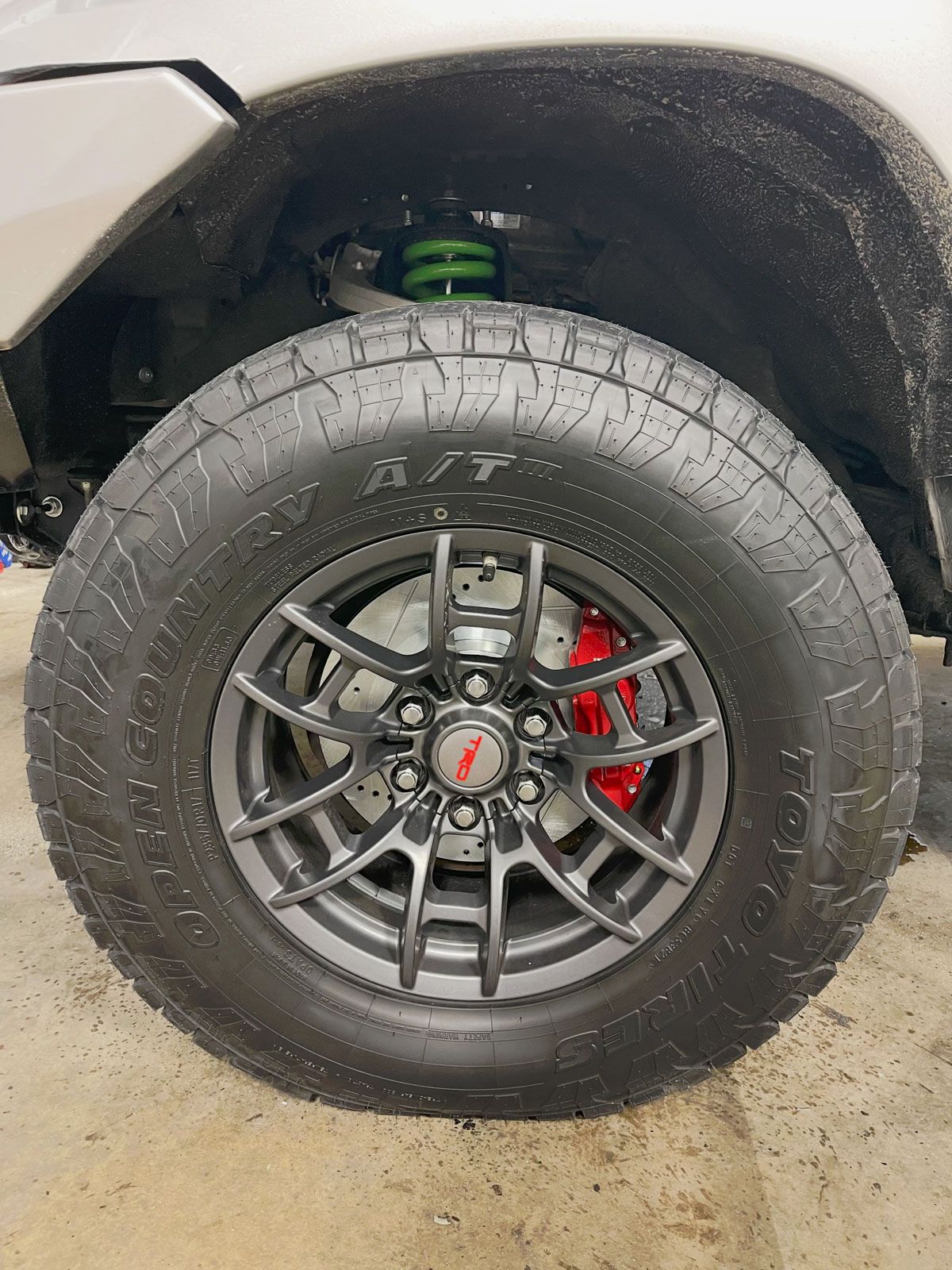 Close-up of a truck wheel with black rim, red brake caliper, and green suspension visible in the wheel well