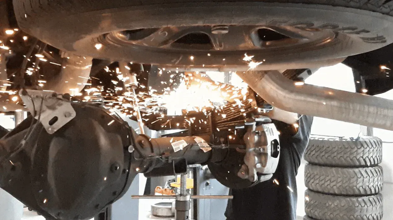 Mechanic grinding under a vehicle, sending sparks in an auto repair shop