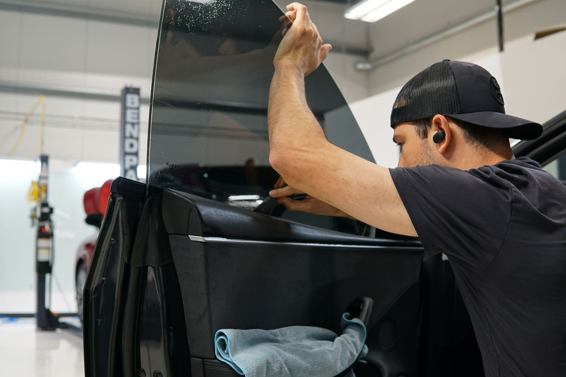 Person applying black window tint to a car in a workshop