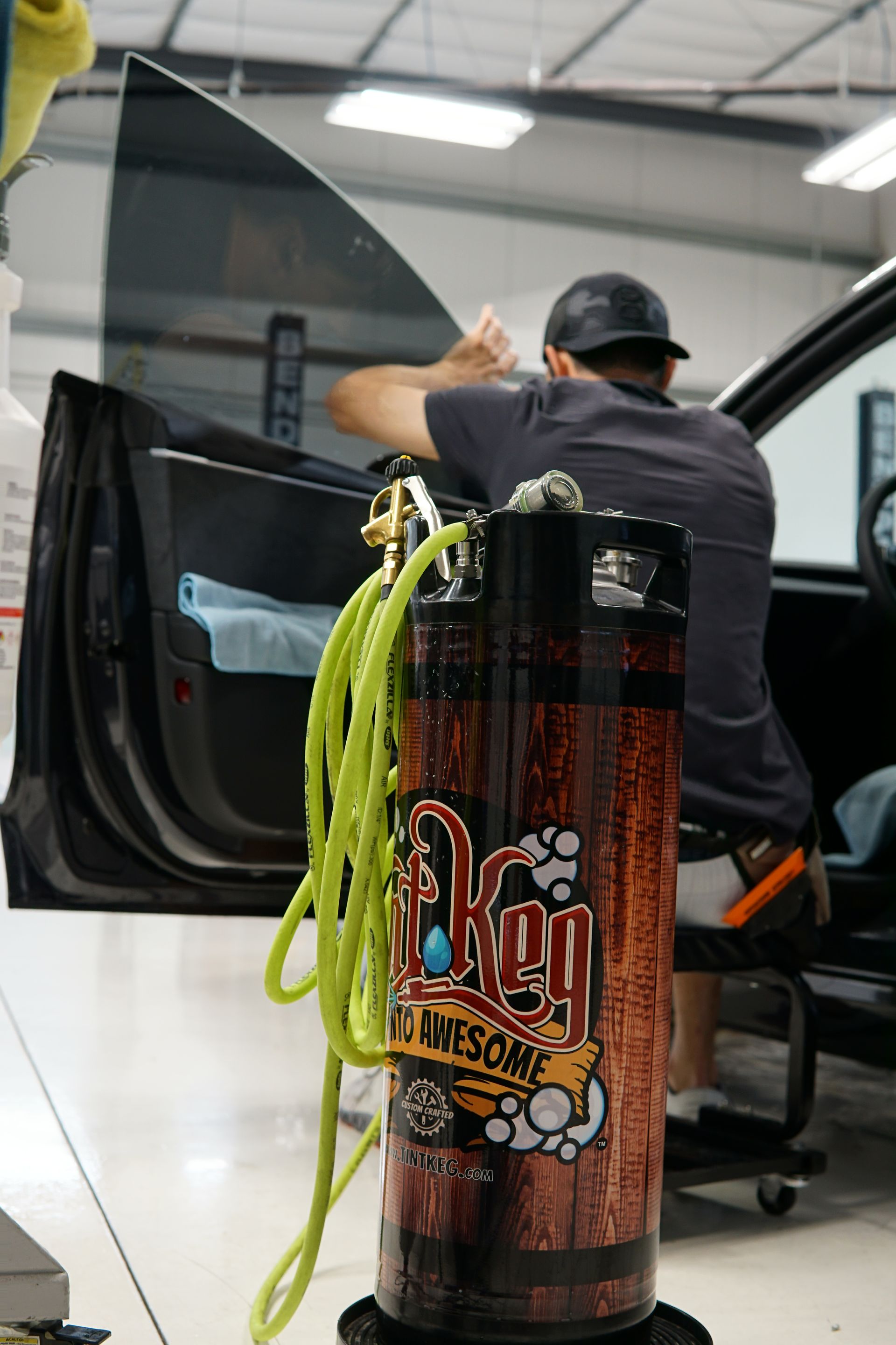Man in a shop detailing a car beside a large bottle of BnE glass cleaner for oversized wheels