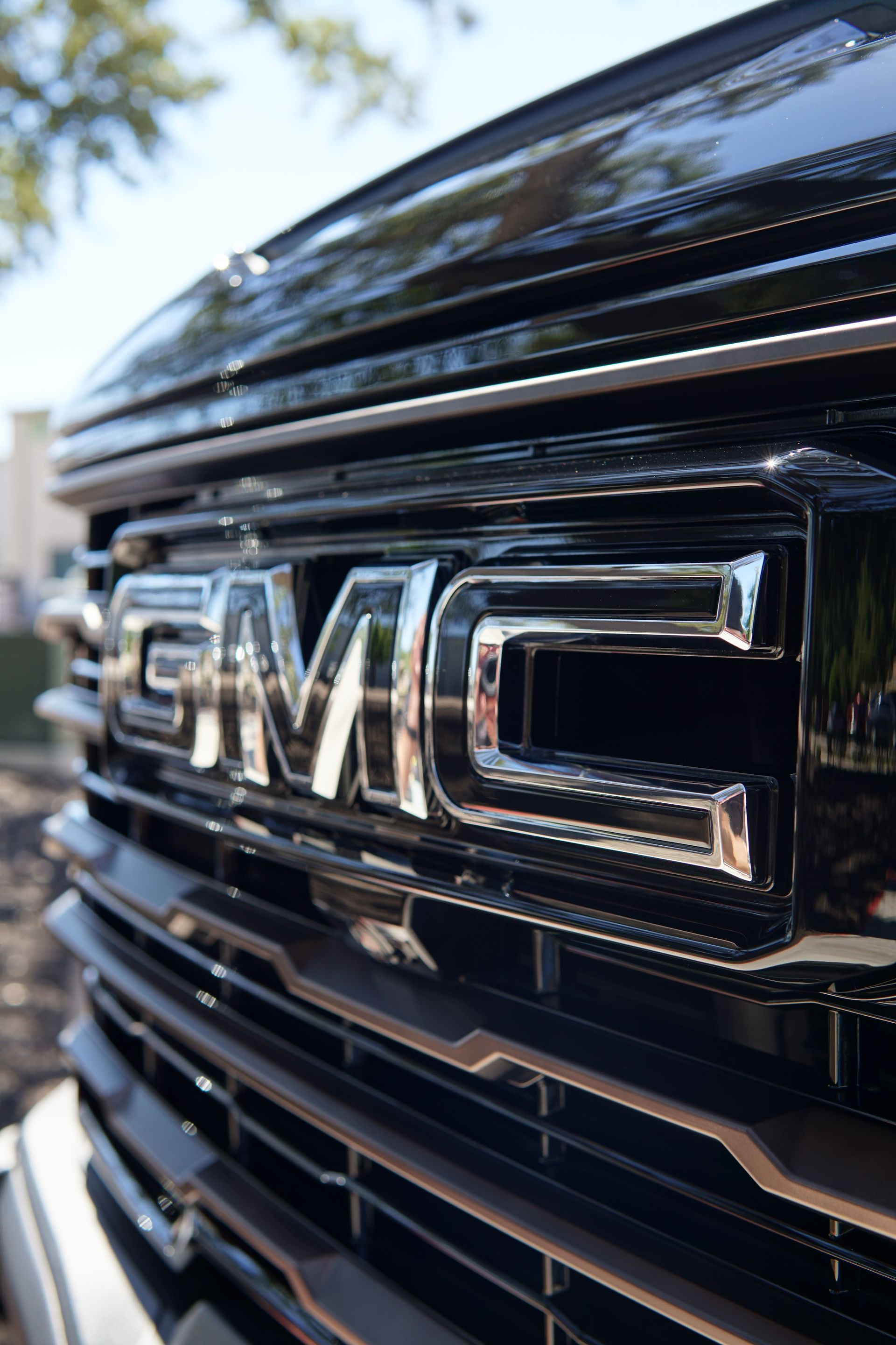 Close-up of a chrome GMC emblem on a glossy black vehicle grille.