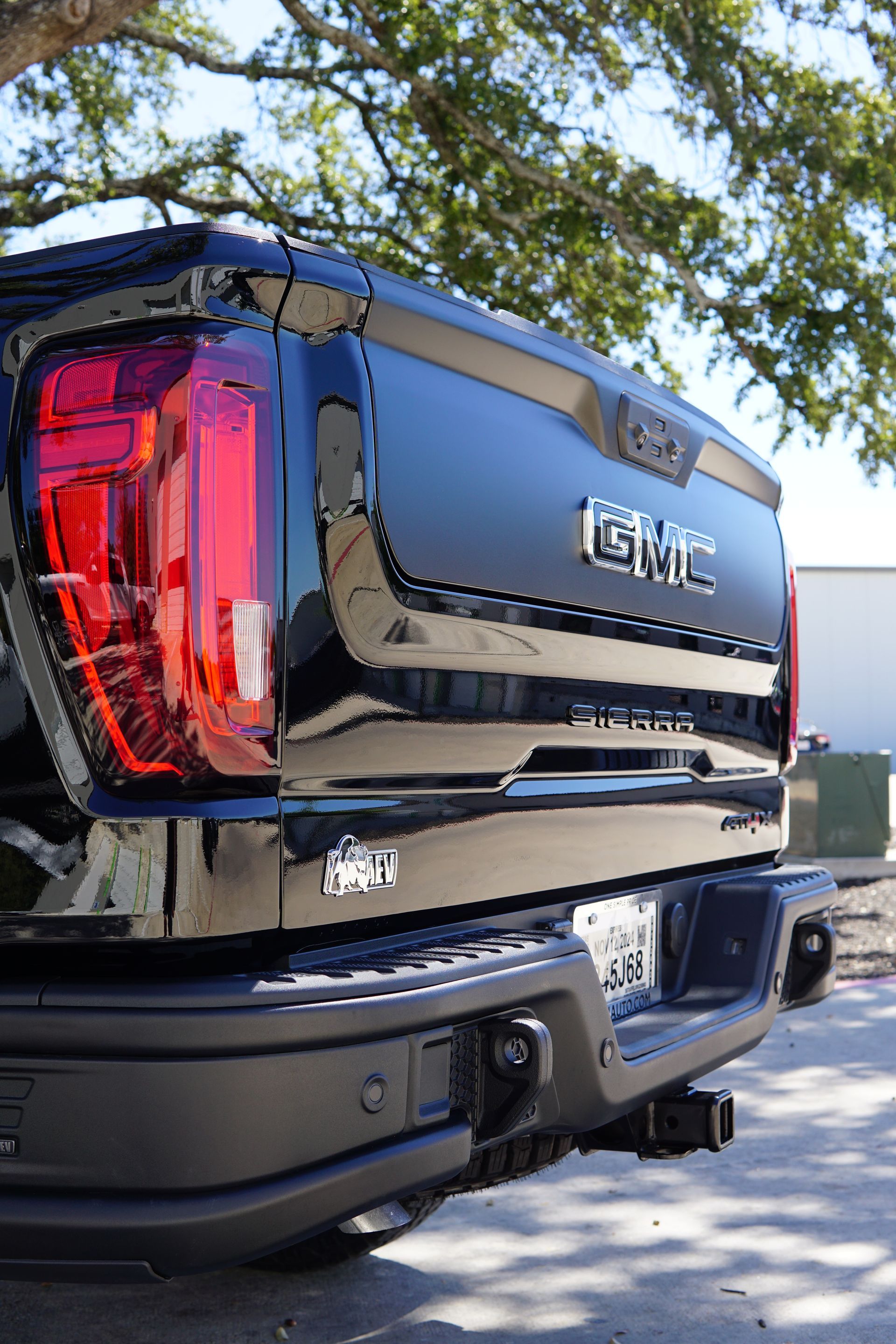 Black GMC pickup truck rear view parked outdoors under trees.