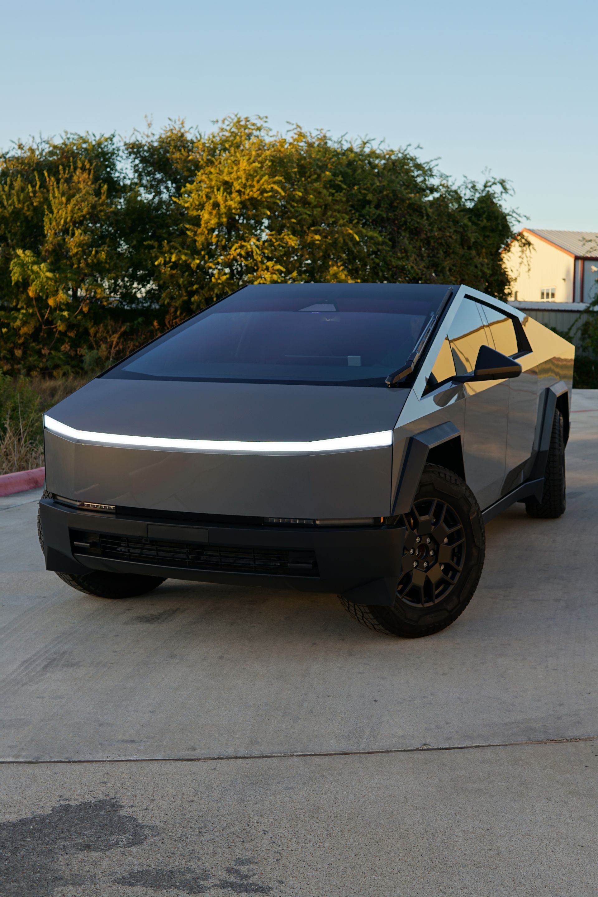 Tesla Cybertruck parked outdoors on a driveway at sunset, silver body with black wheels.