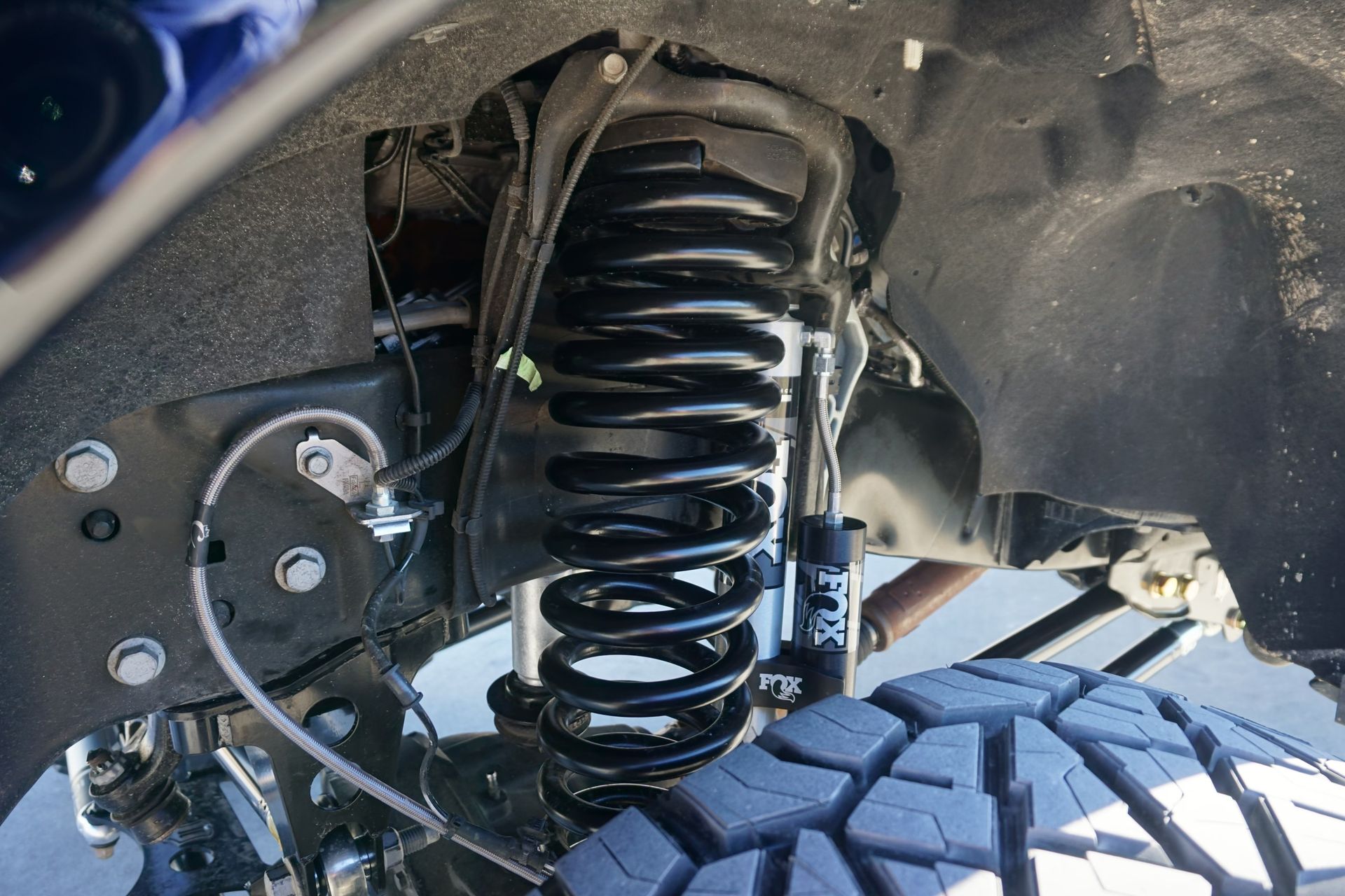 Close-up of a black vehicle suspension coil spring and off-road tire under the wheel well
