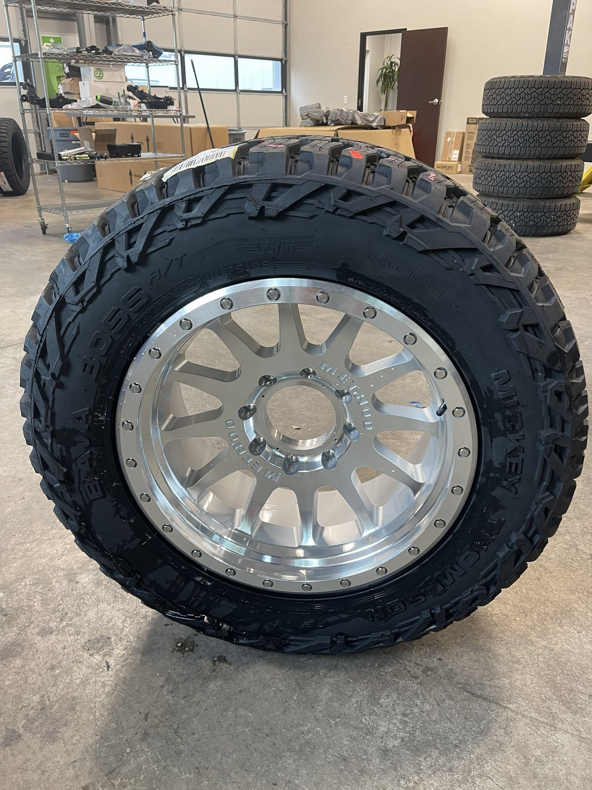 Black pickup truck lifted in a garage, with one front wheel removed and exposed brake assembly.