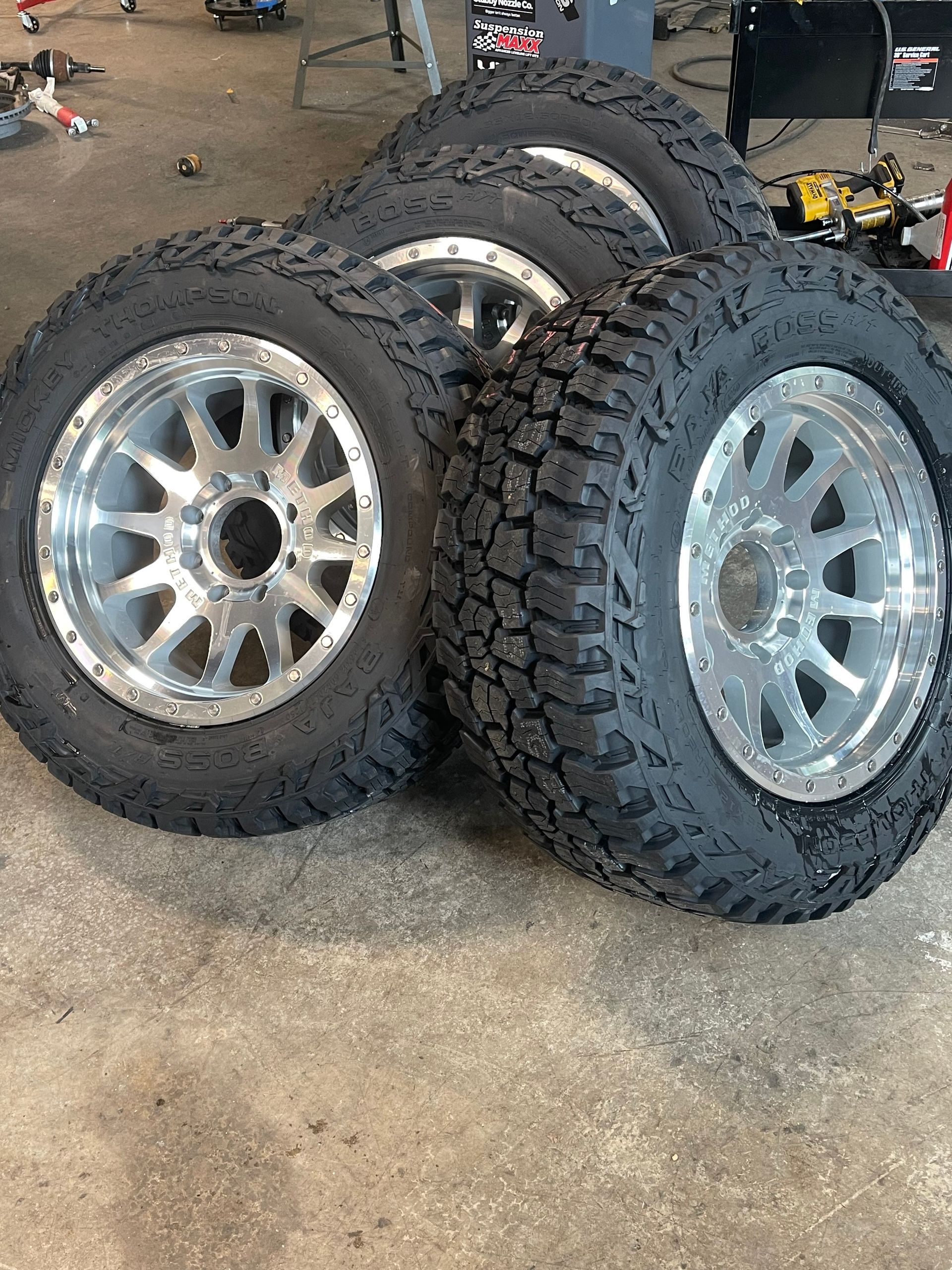 Three off-road tires with silver rims stacked in a workshop garage.