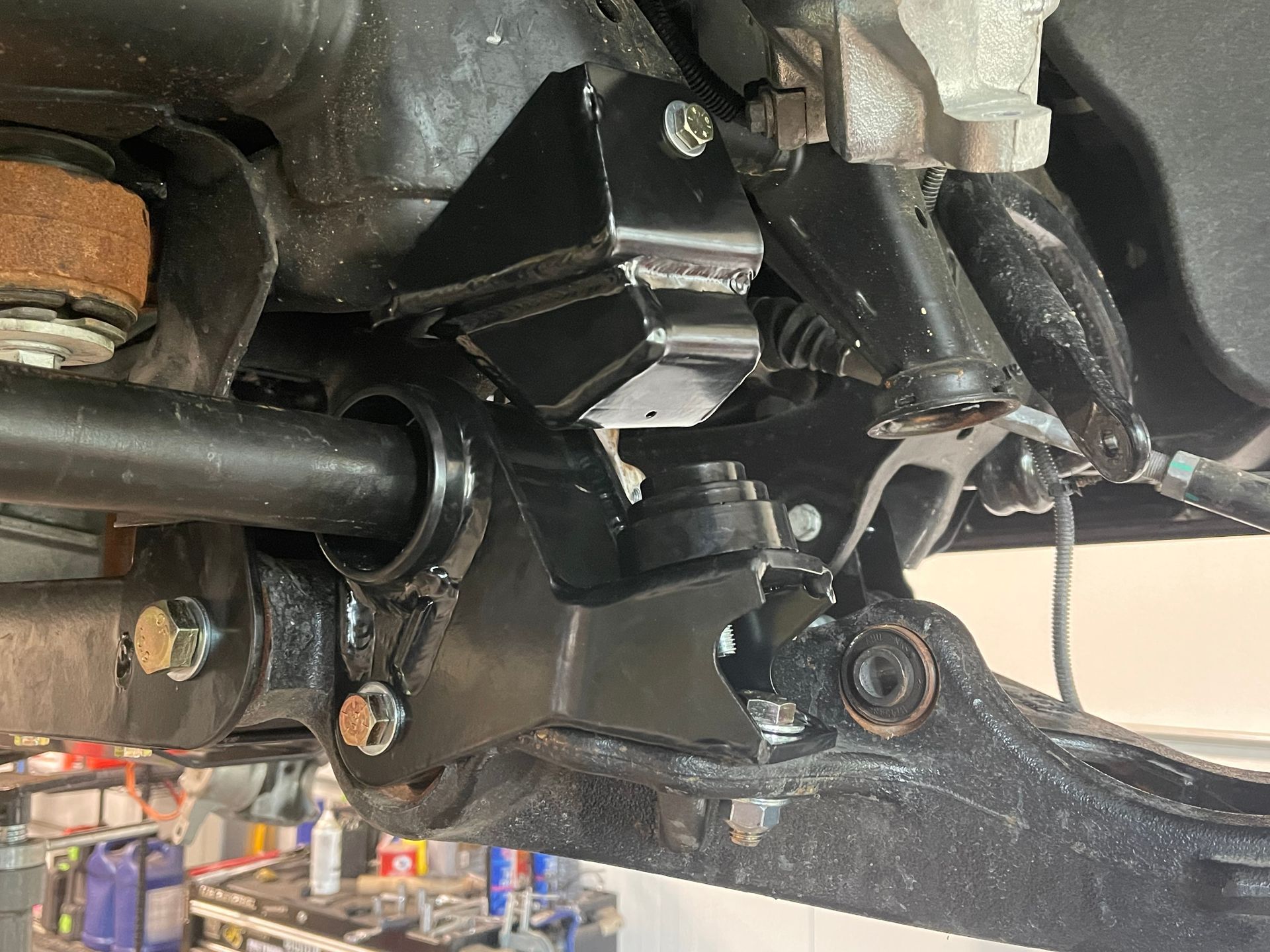Close-up of a black metal vehicle suspension and drive shaft undercarriage with bolts and brackets
