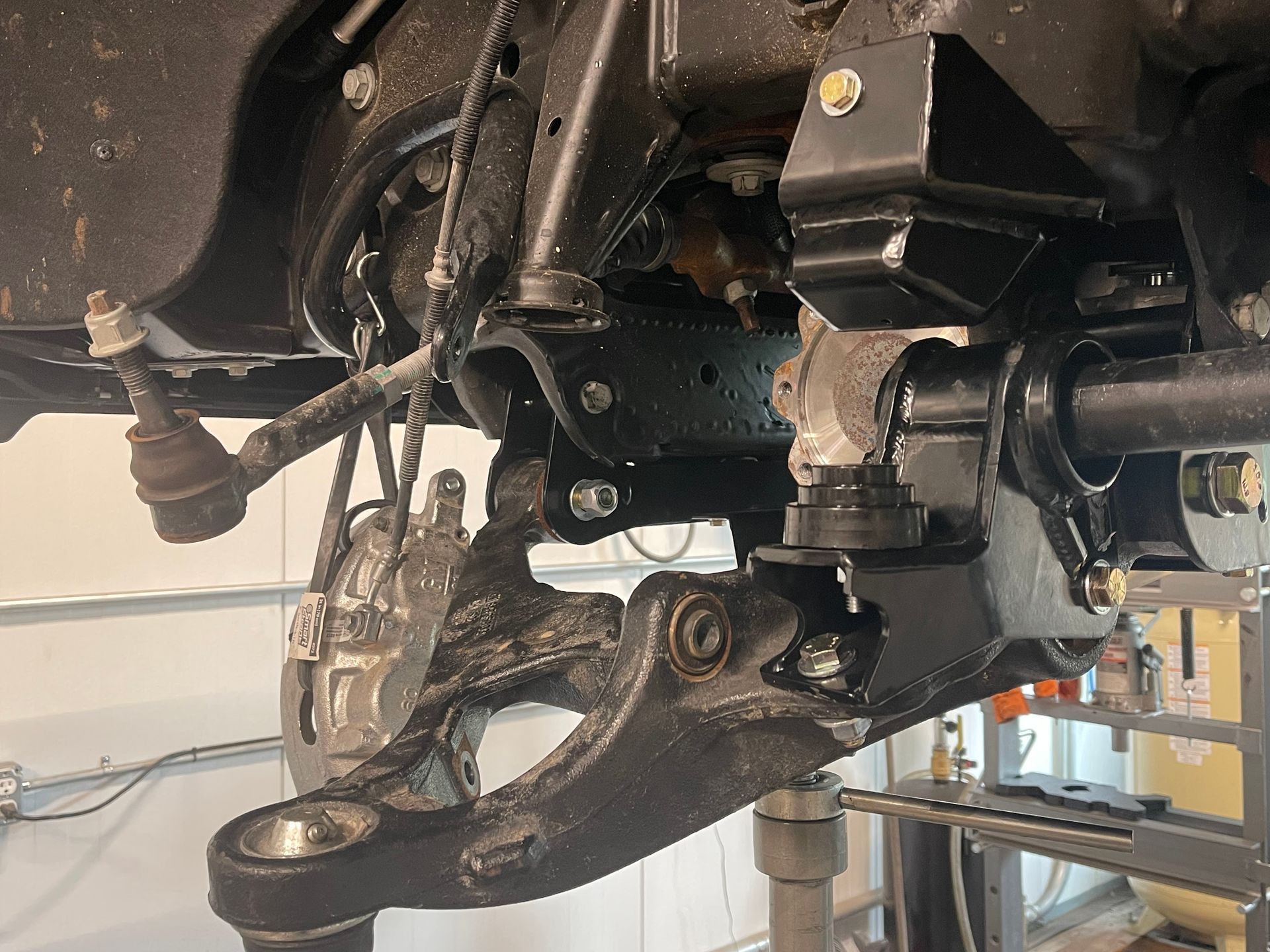 Close-up of a vehicle suspension and axle assembly with black metal parts in a workshop.
