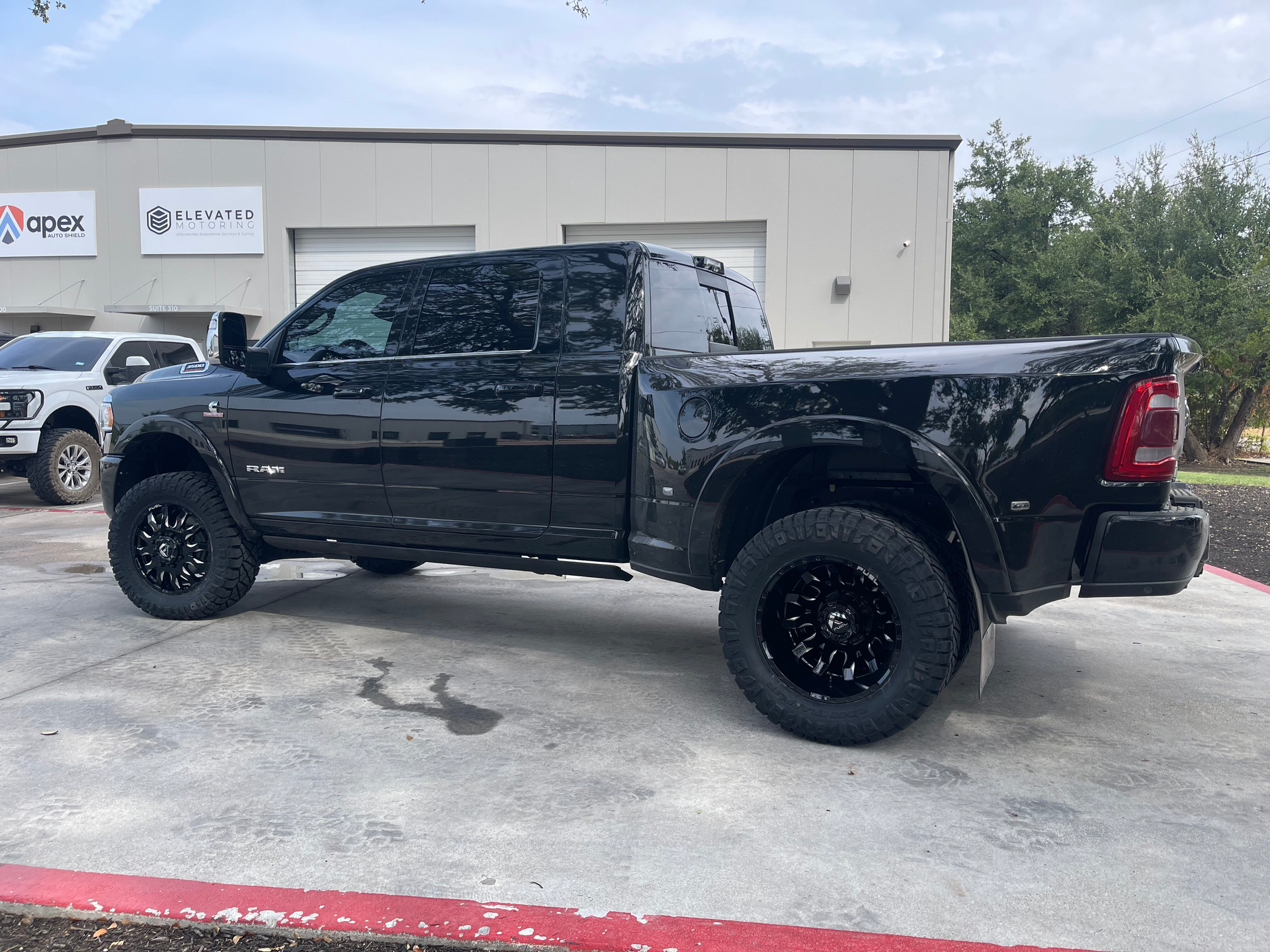 Black lifted pickup truck parked outside a storefront on a cloudy day