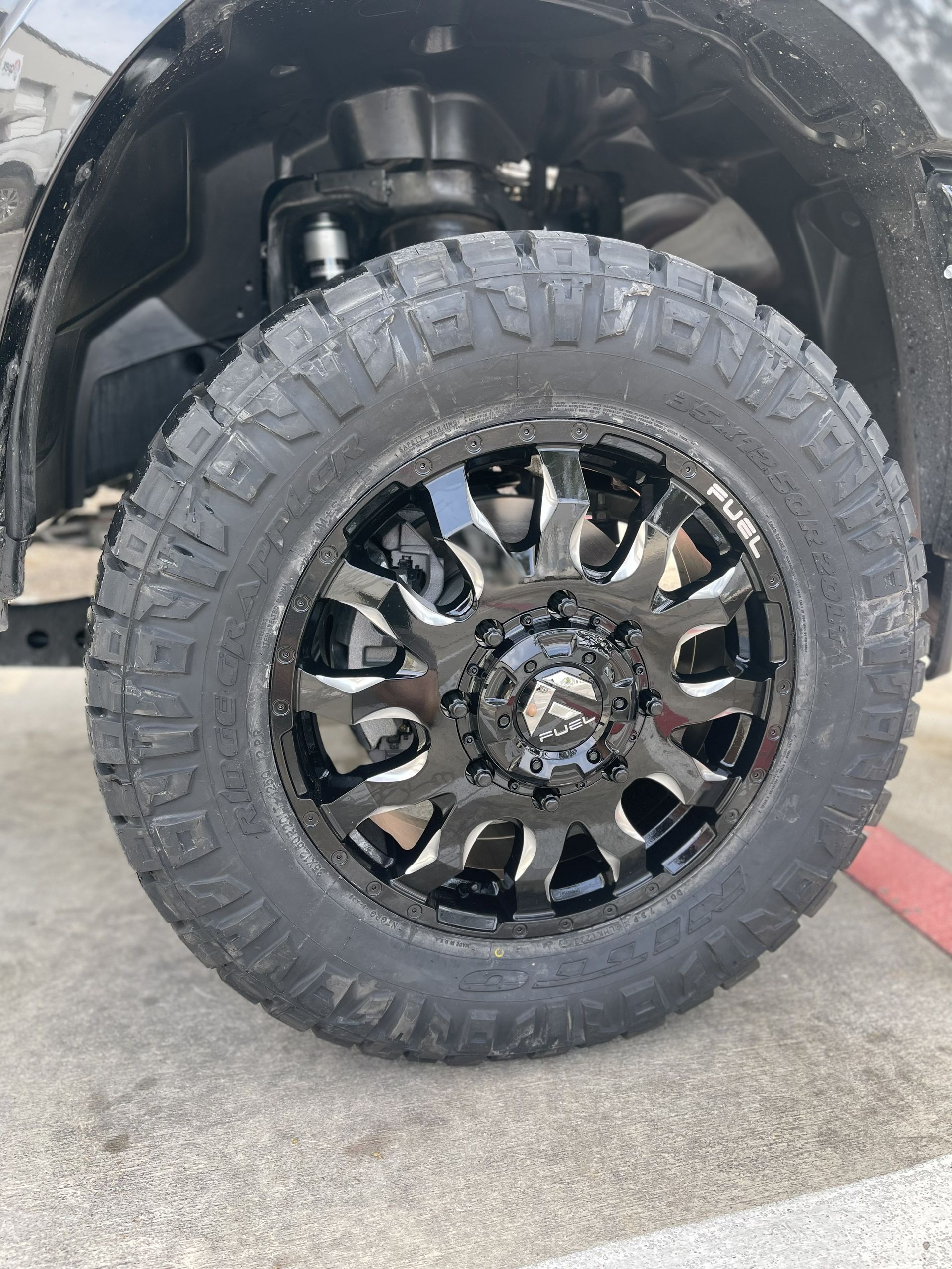 Close-up of a black off-road truck tire with chrome rim parked on concrete.