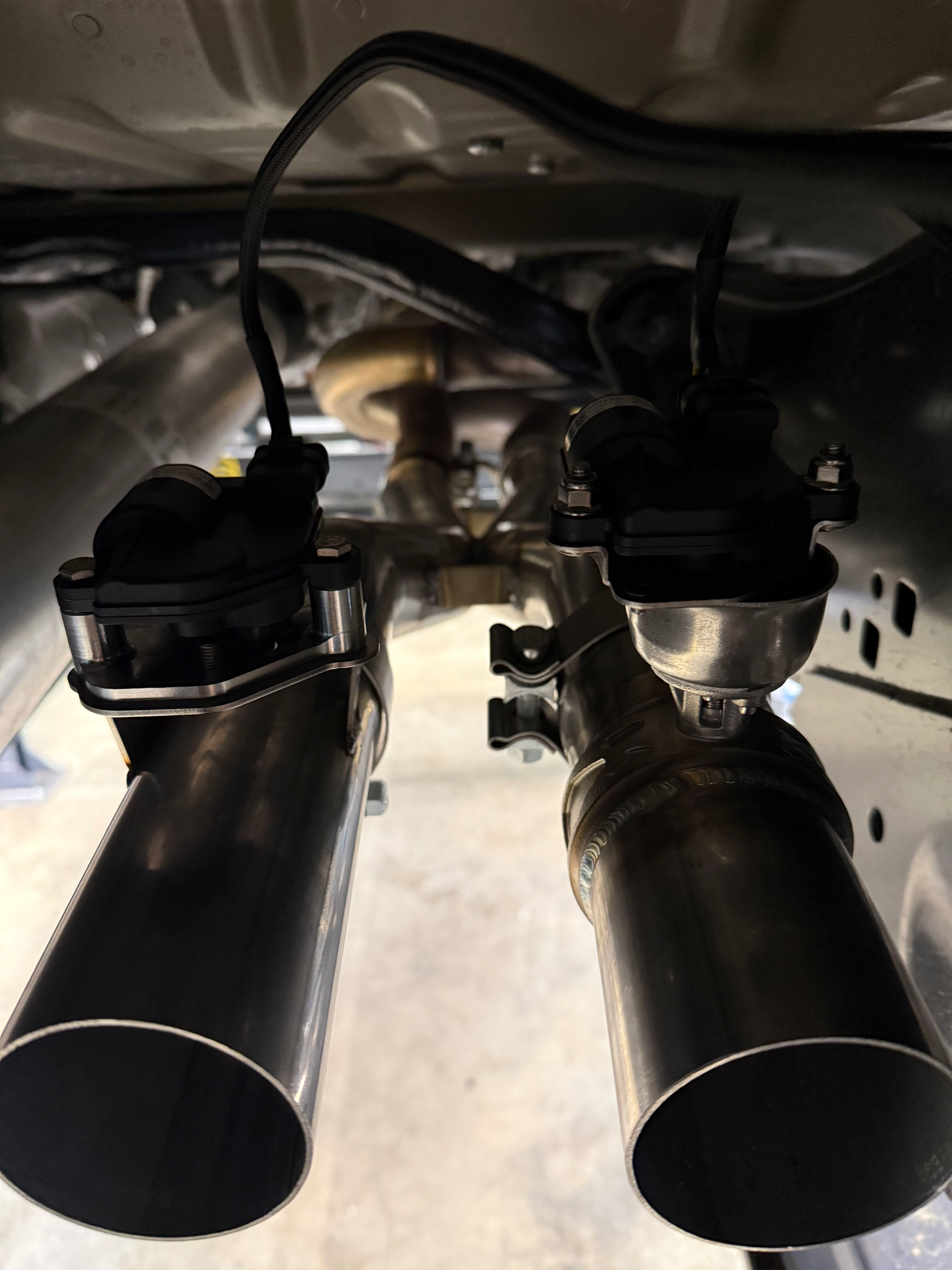 Dual exhaust pipes under a vehicle, showing the muffler and hanging hardware.