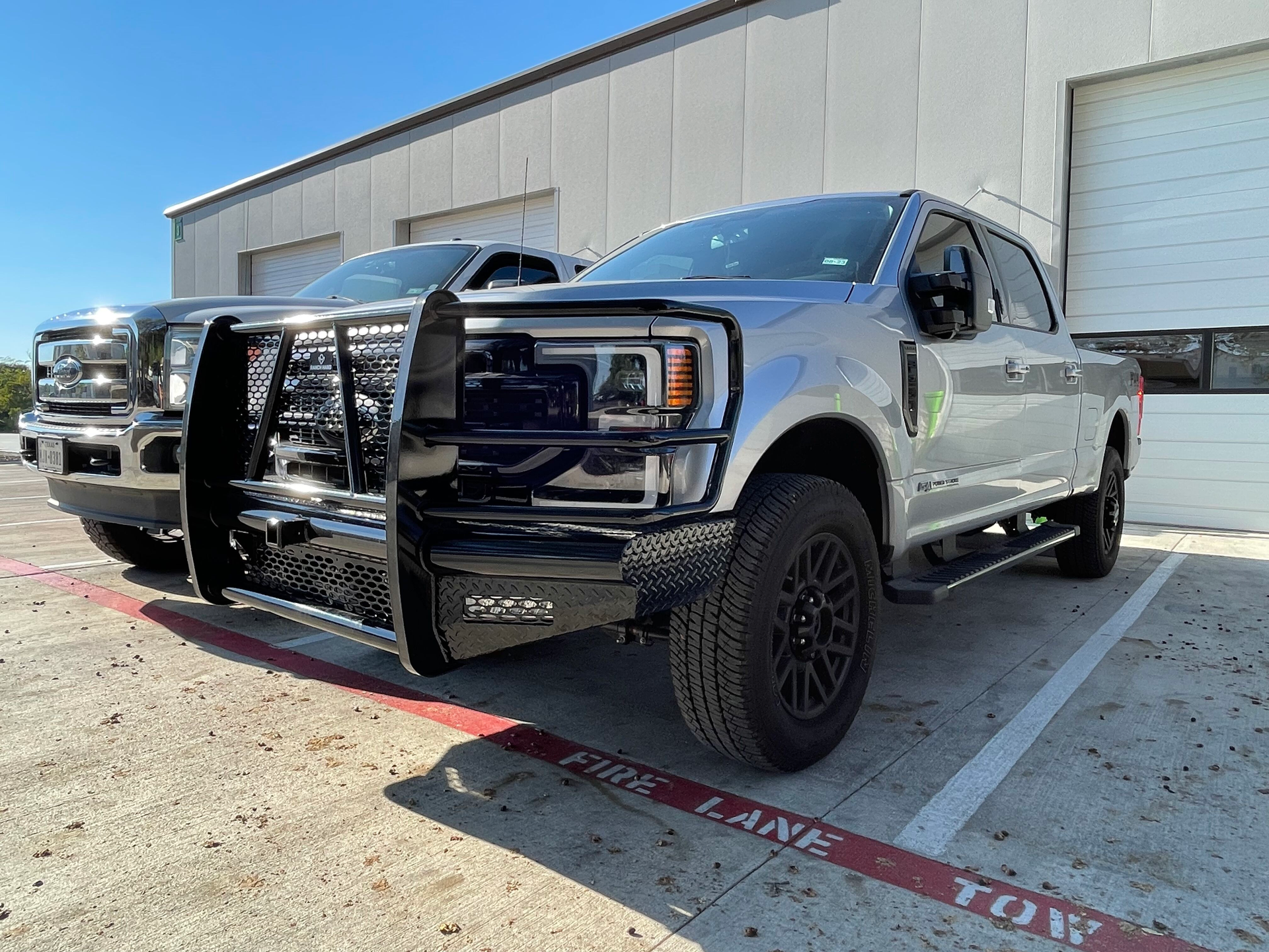 Black pickup truck with a snowplow parked outside a warehouse loading dock.