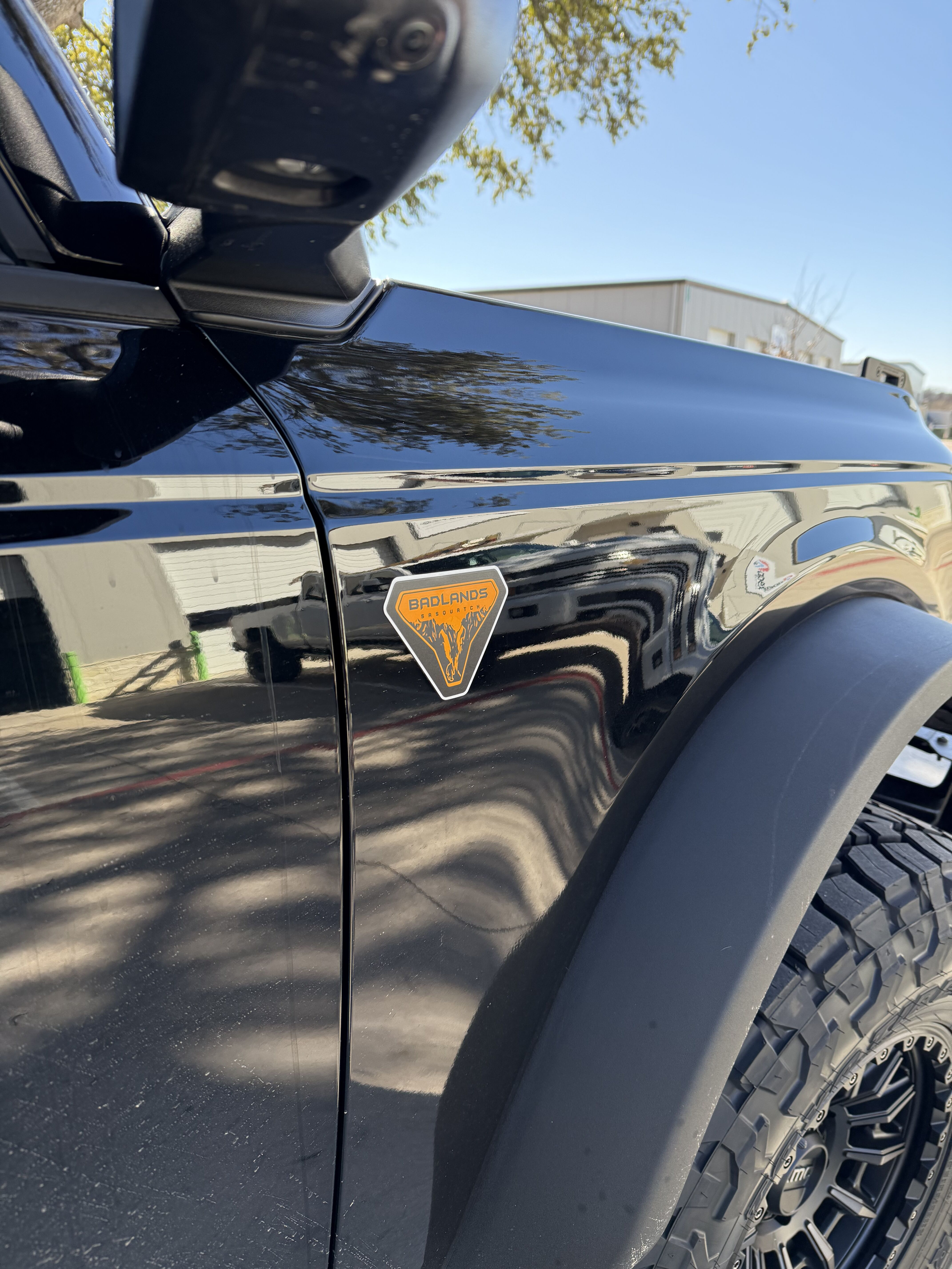 Close-up of a black off-road truck with orange badge and rugged tire in a driveway