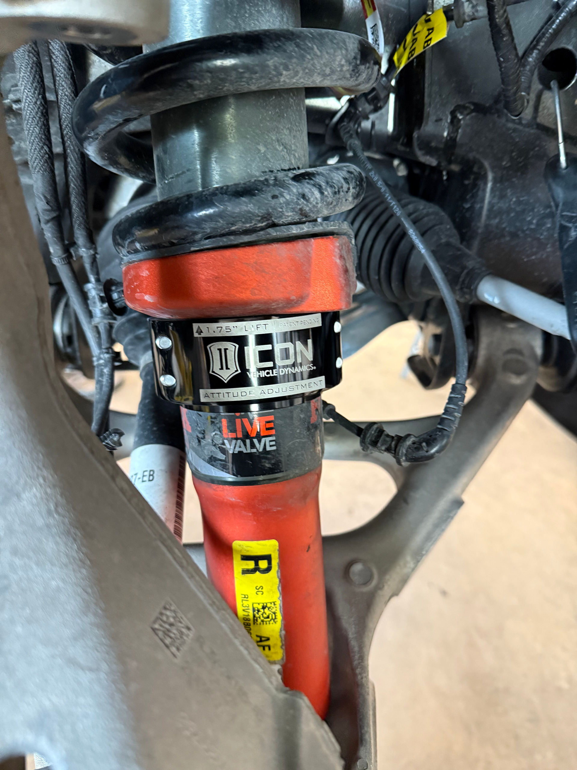 Close-up of an orange motorcycle shock absorber with black suspension parts and wiring.