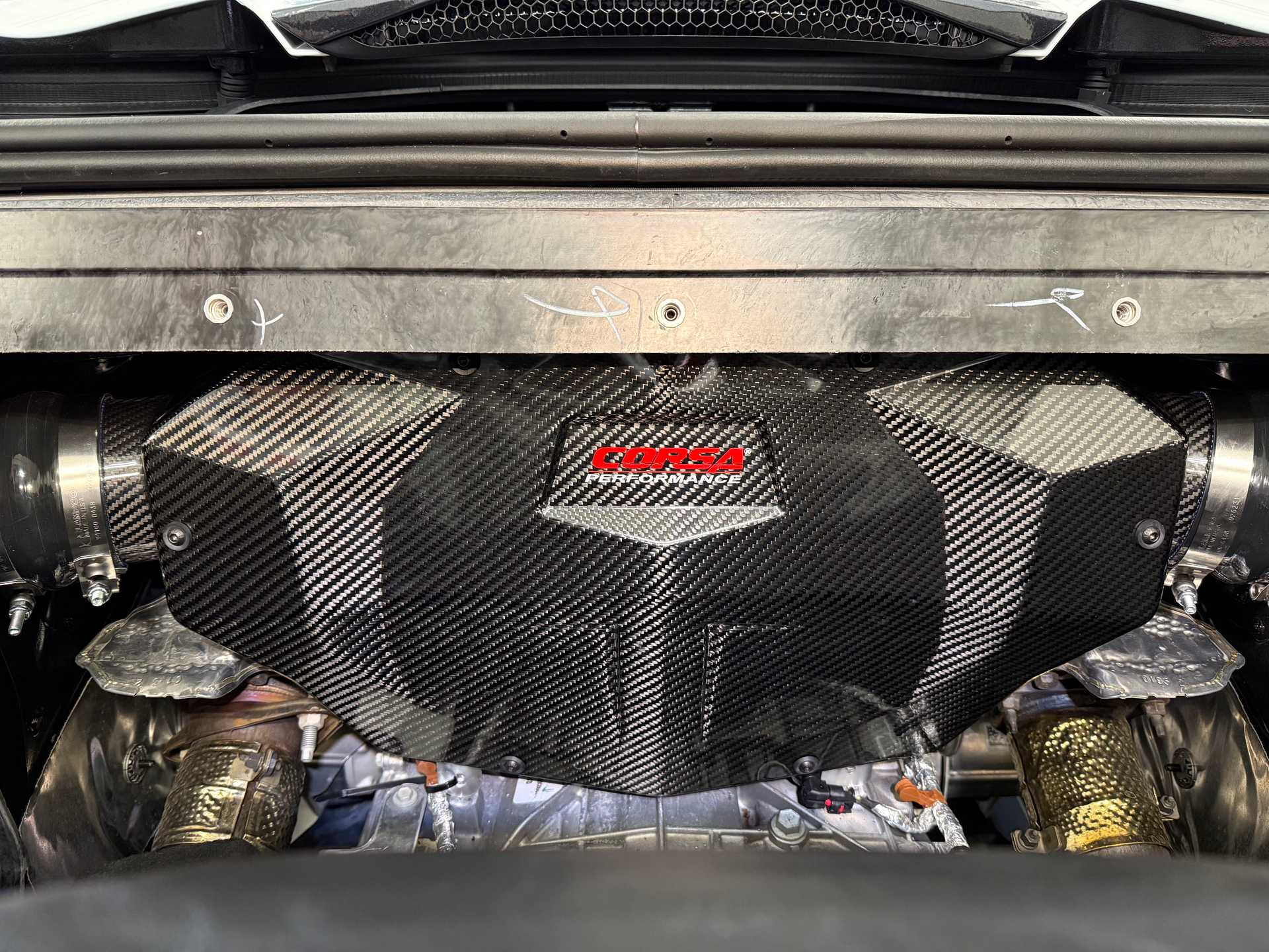 Carbon-fiber engine bay cover with red logo, seen from the rear of a car.