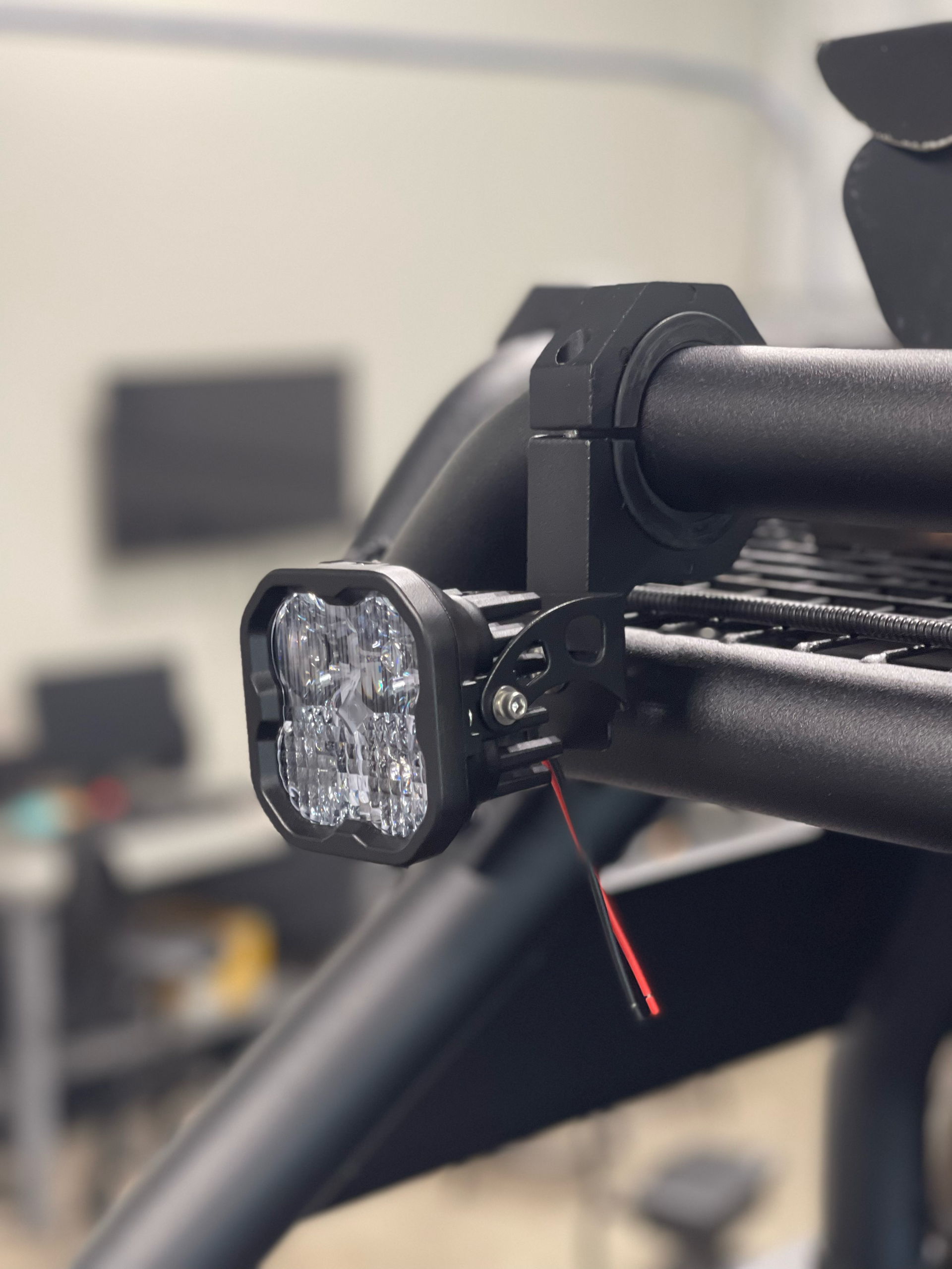 Close-up of a mounted square LED light on a black metal frame with a red wire attached.