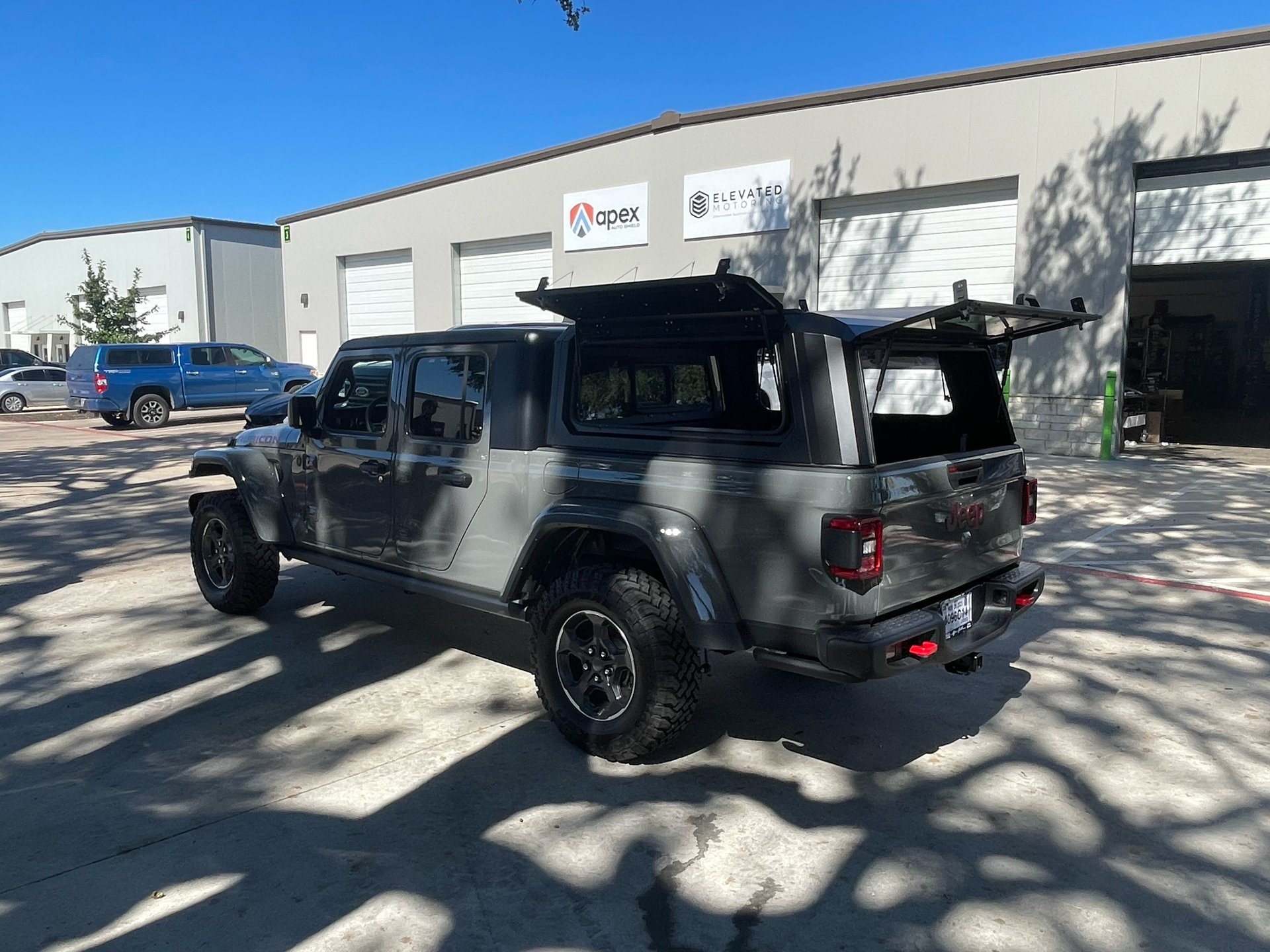 Black Jeep Gladiator parked outside a light industrial building in sunny daylight.