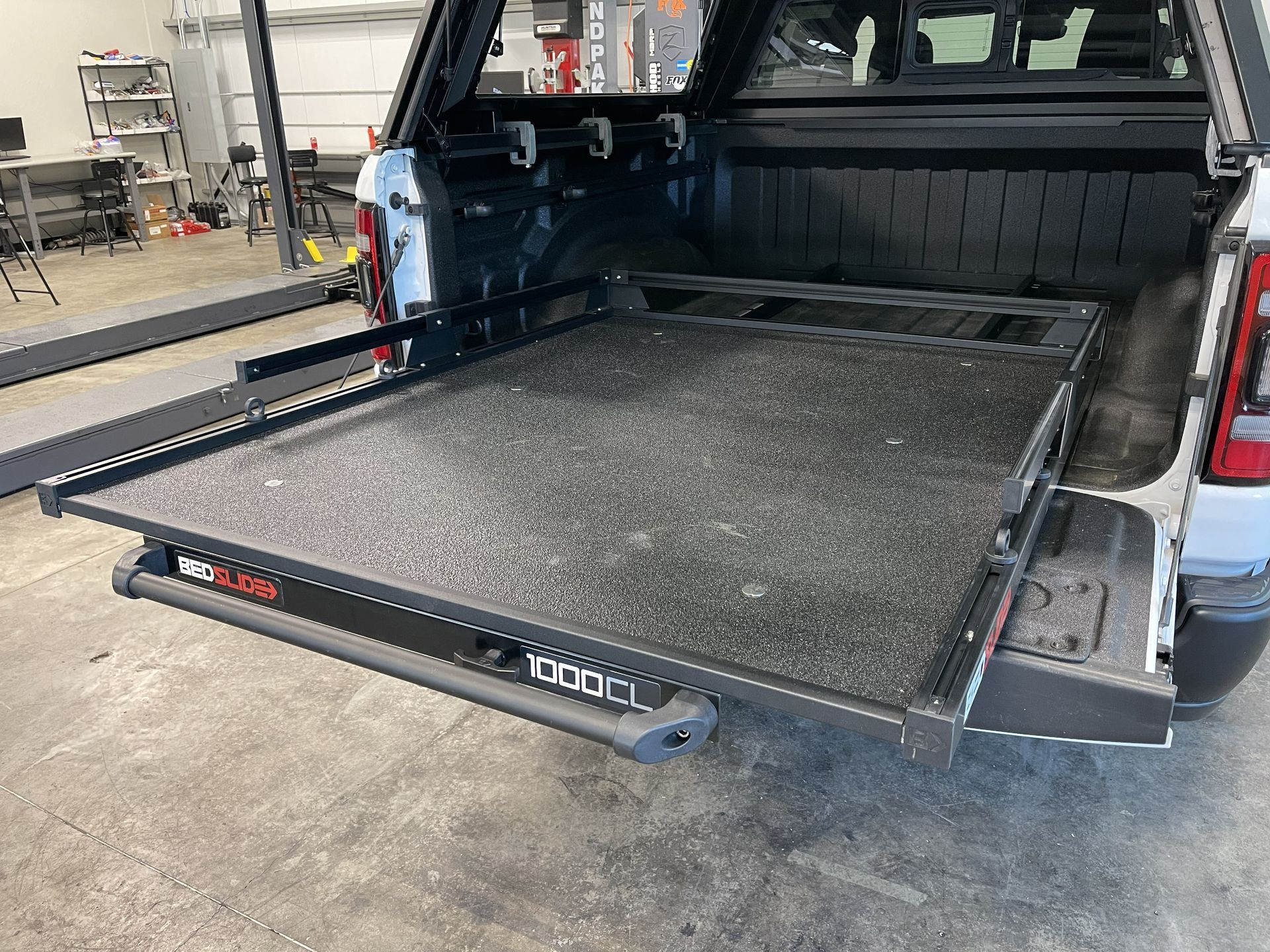 Pickup truck with a black fold-down ramp deployed from the open tailgate in a garage.