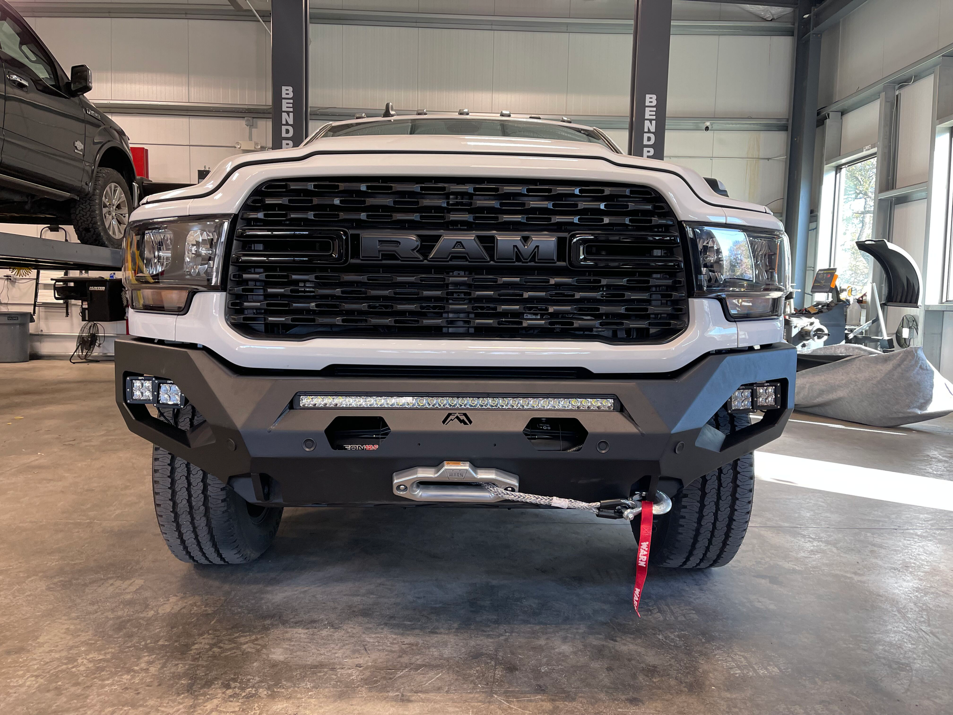 White RAM pickup truck parked inside a garage, front view with black grille and red tow strap