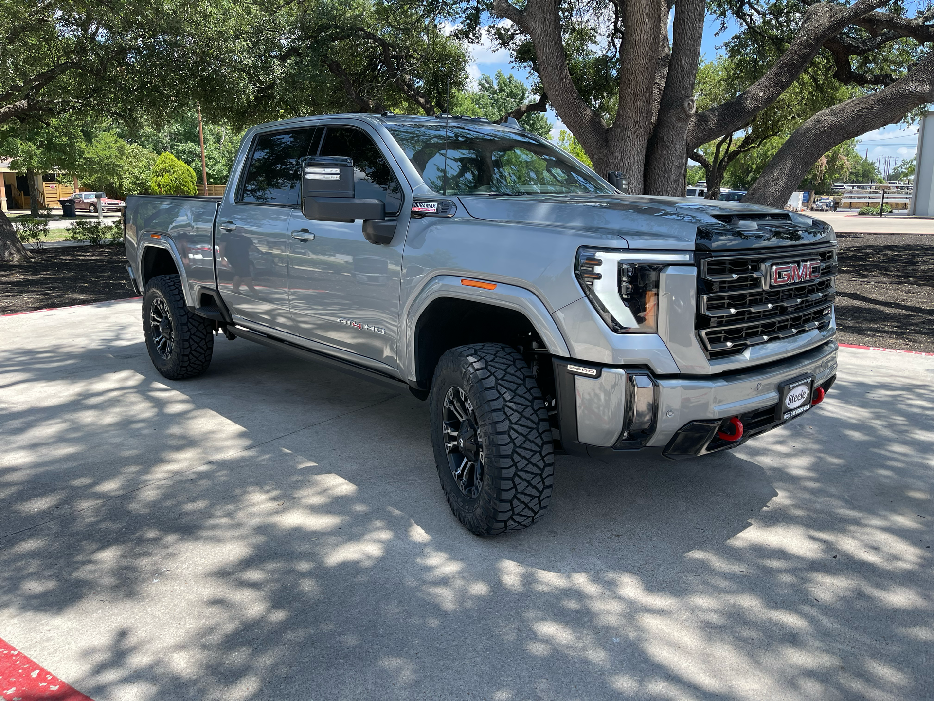 Silver pickup truck parked under trees on a sunny street, front three-quarter view