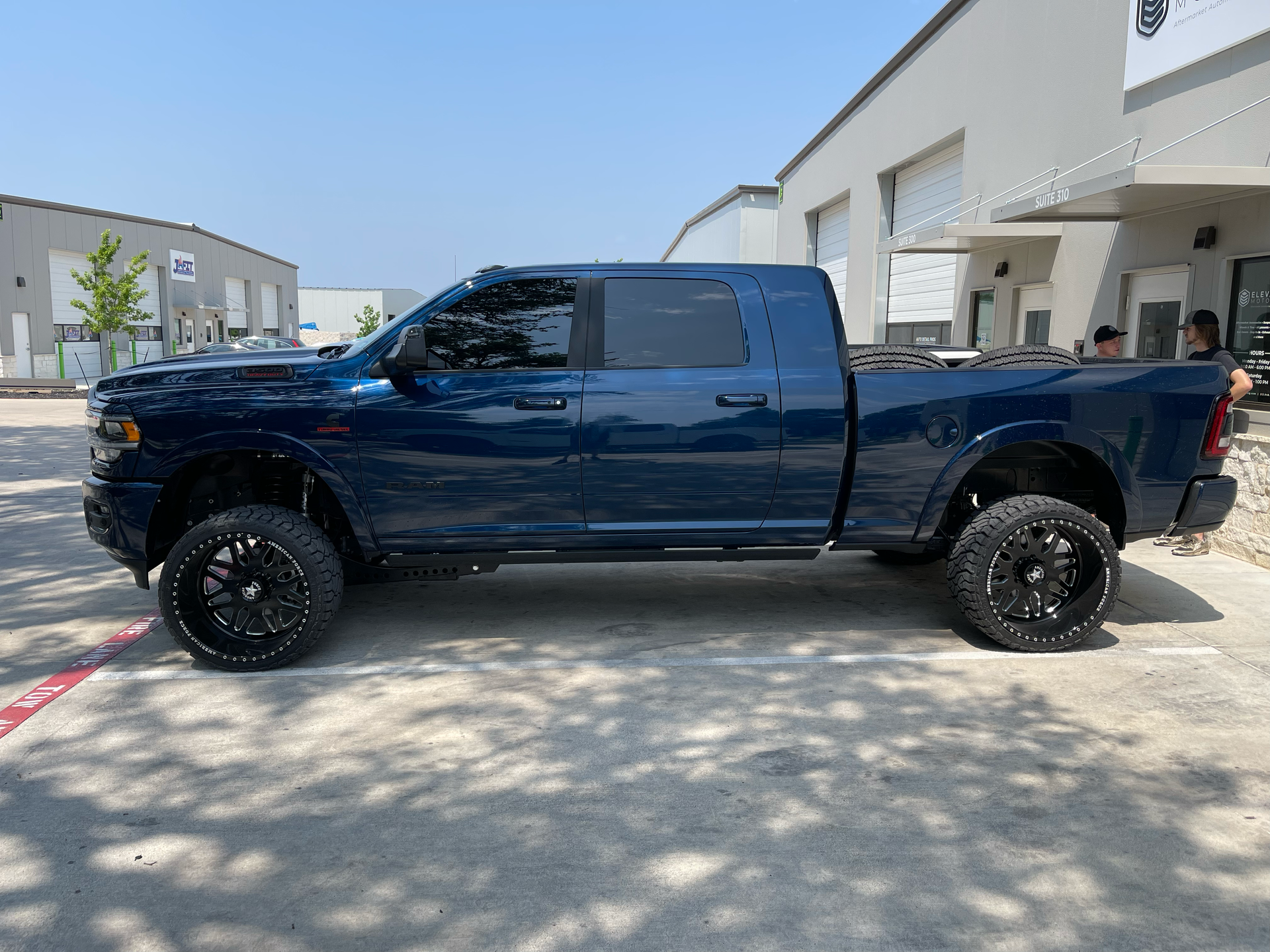 Dark blue lifted pickup truck parked outside a commercial building in sunlight
