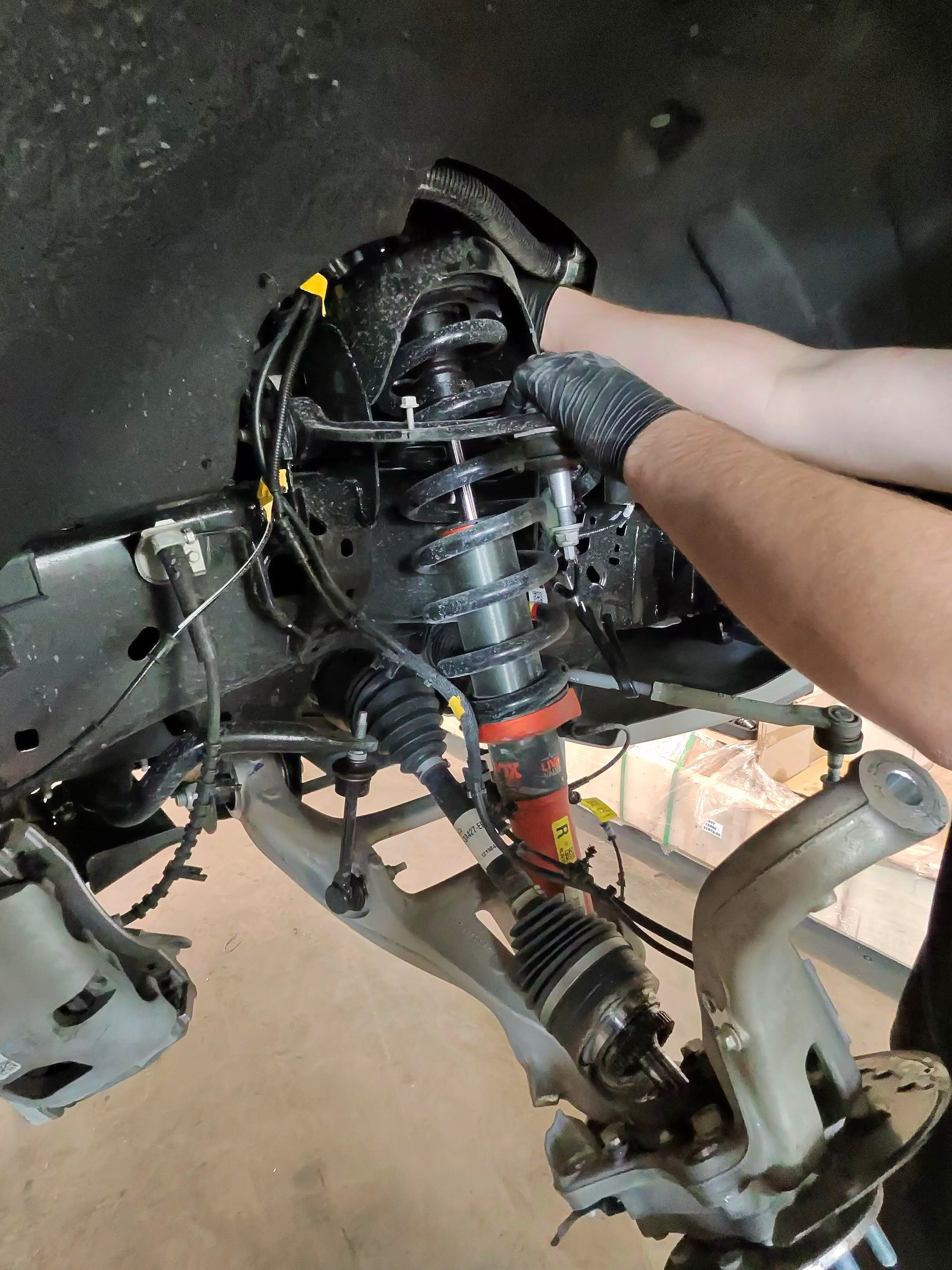Hands working on exposed motorcycle frame and engine in a garage, with tools and parts nearby