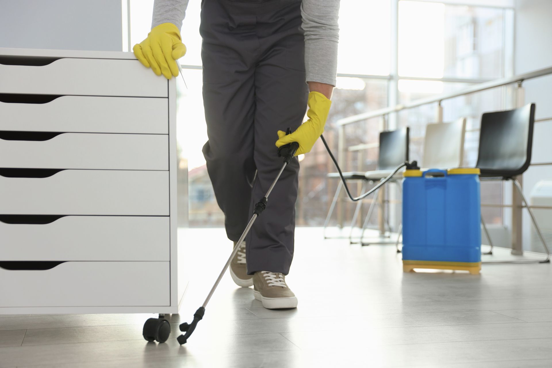 Termite extermination technician spraying baseboards indoors wearing gloves and protective gear.