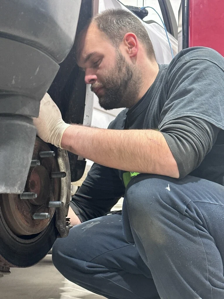 Mechanic working on a car wheel, wearing gloves, in a garage. | Your Buddy Steve's Garage