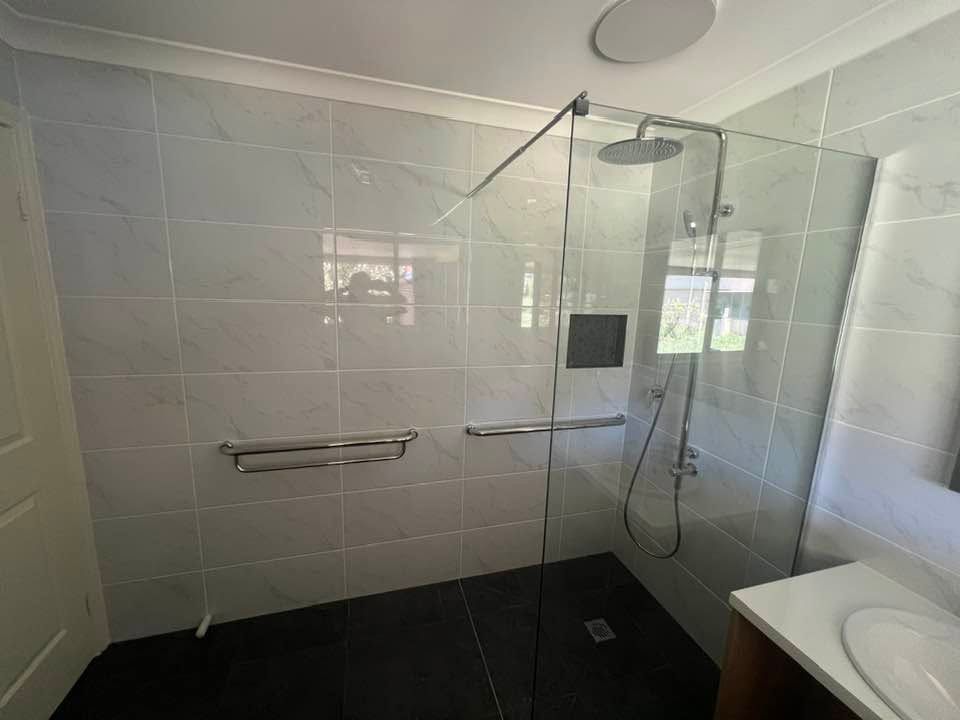 Modern Bathroom With A Glass Walk-in Shower, White Tiled Walls, And Black Floor Tiles by McGrath Builders & Associates in Lavington NSW.