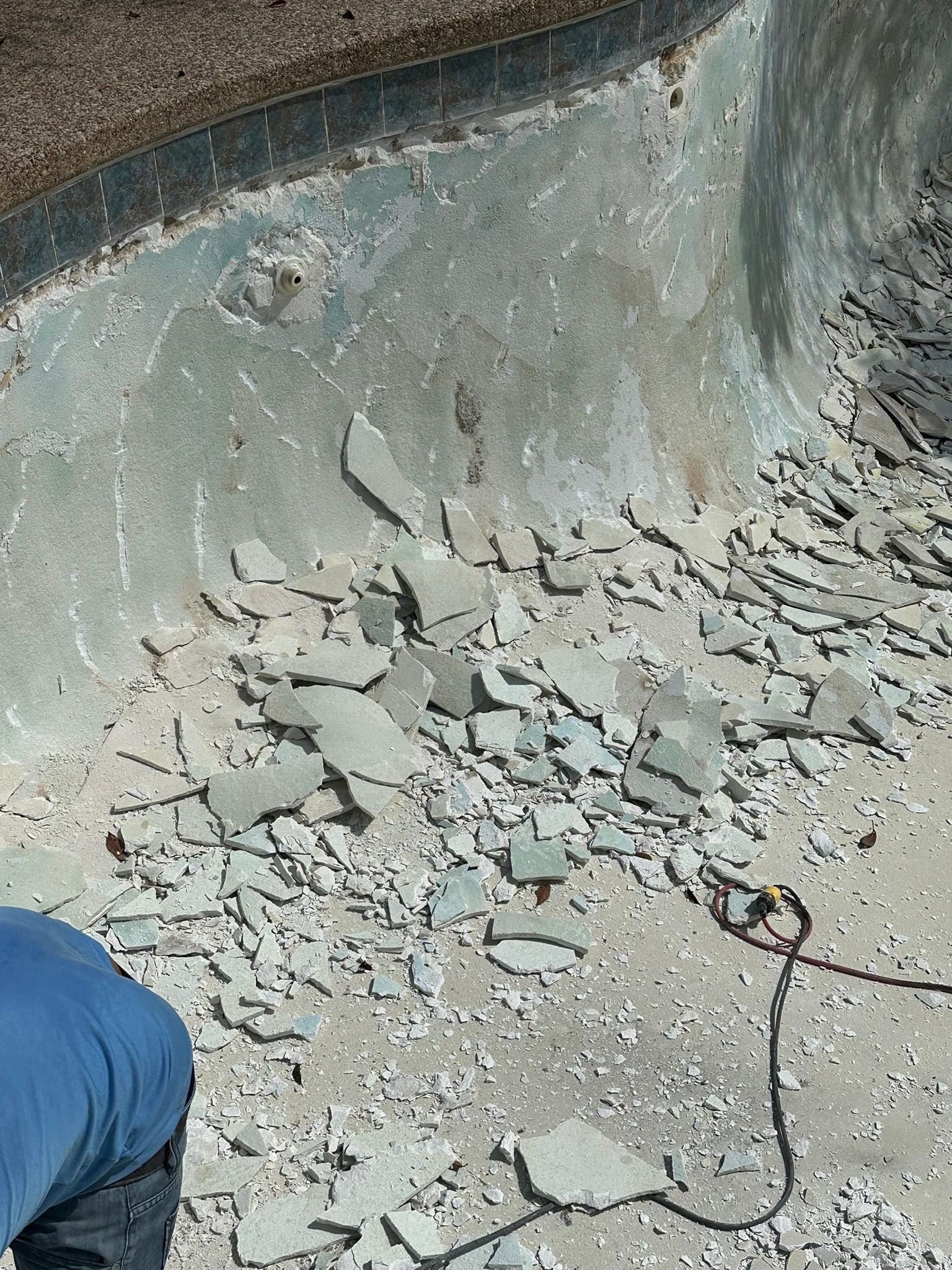Pool interior with chipped surface and debris; person in blue shirt working.