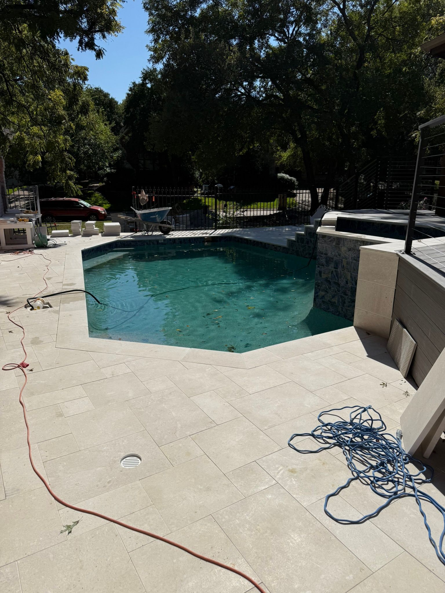 Pool under construction with turquoise water, surrounded by light-colored paving stones. Blue rope and electrical cord in foreground.
