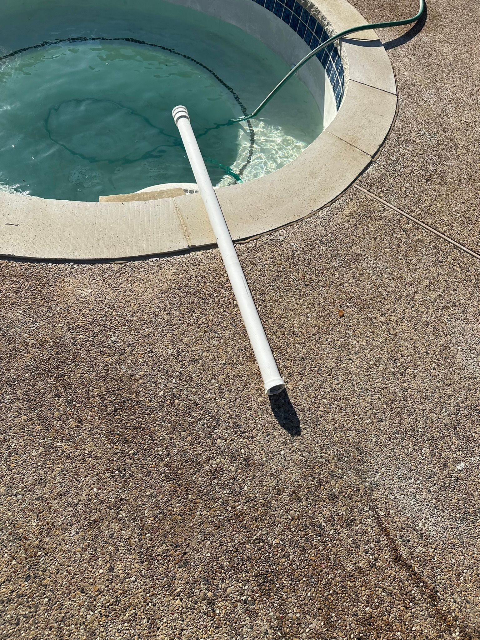White pool cleaning pole resting on speckled concrete next to a pool.