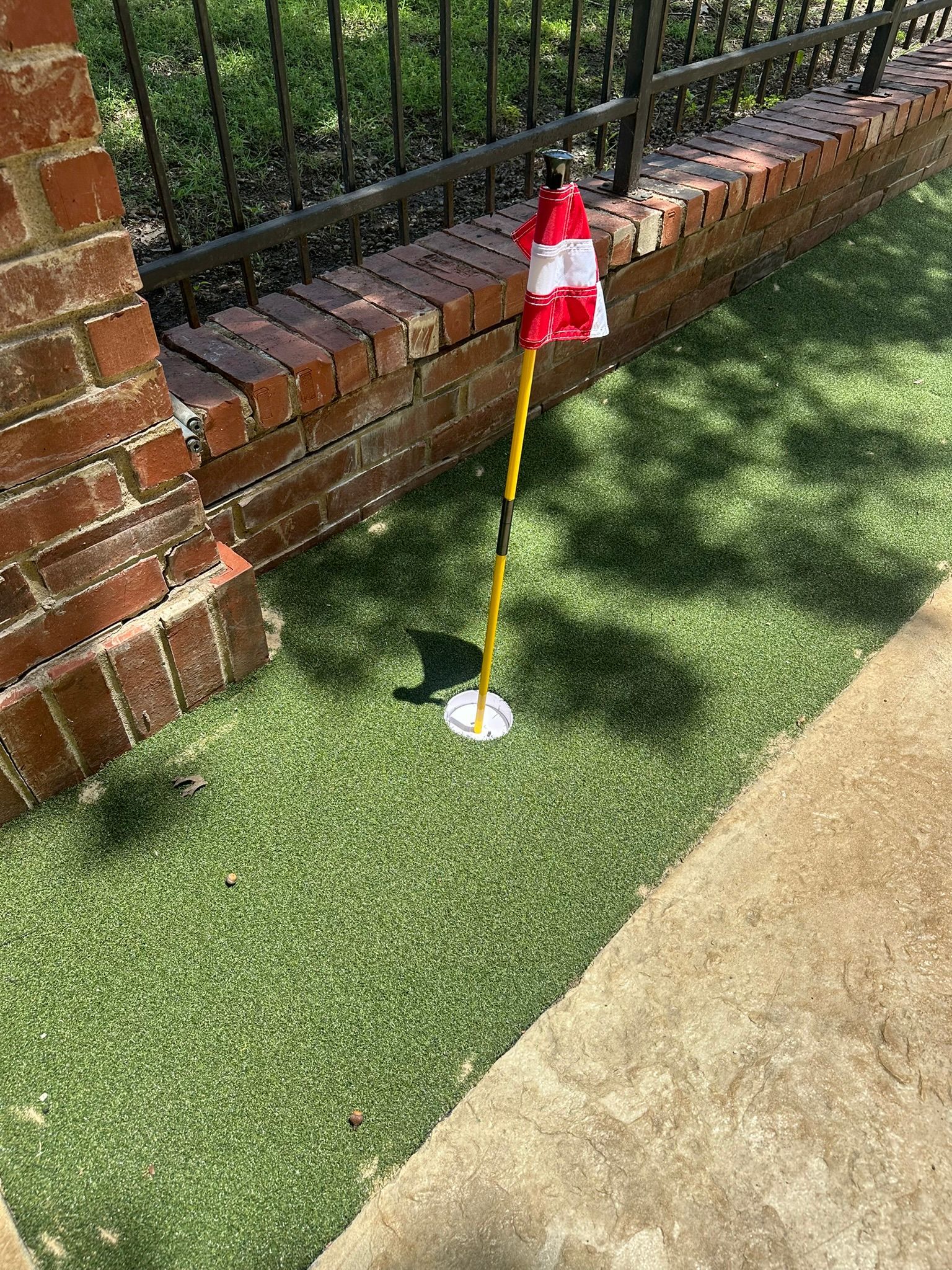 A golf green with a flag next to a brick wall.