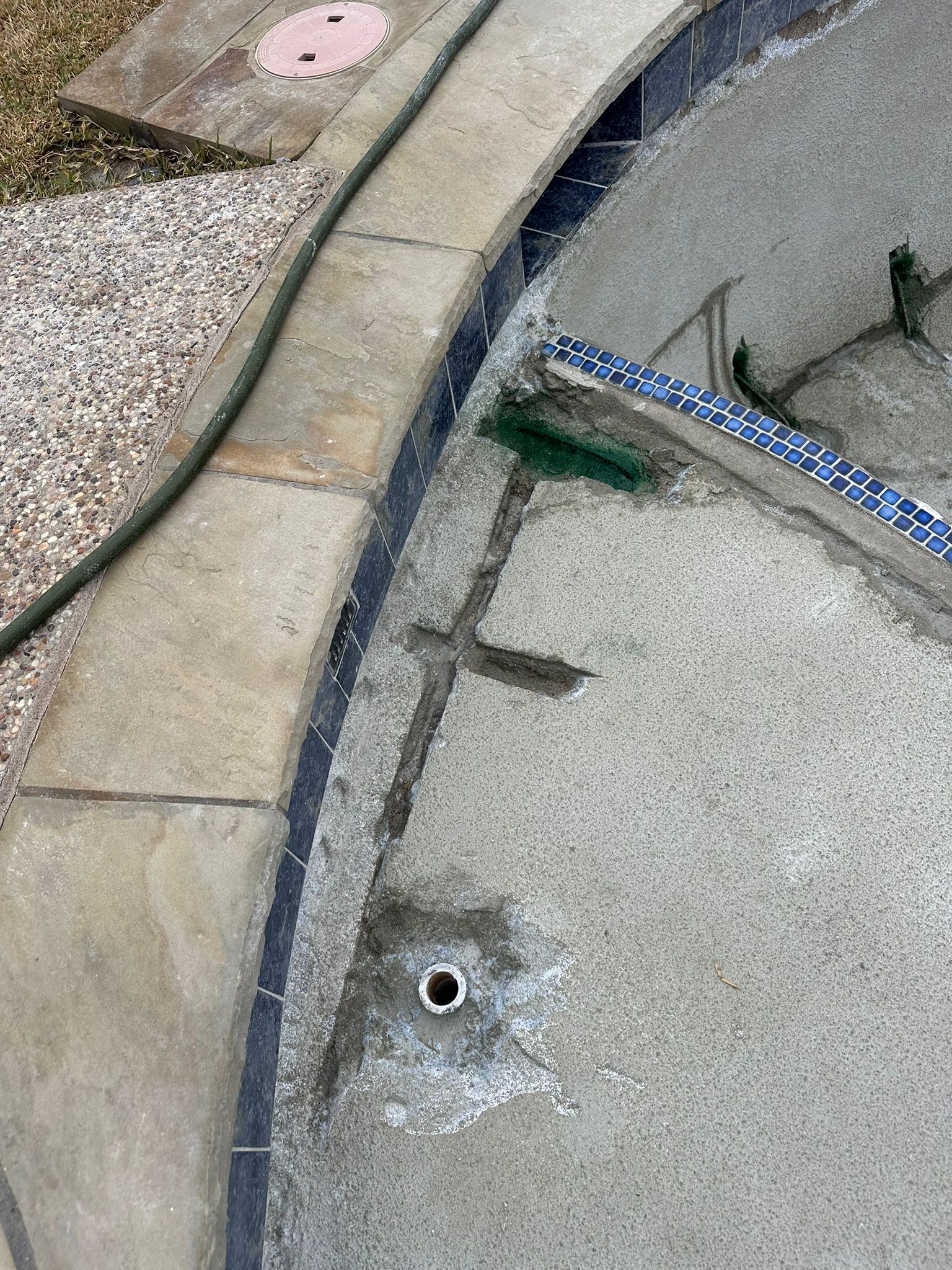 Close-up of a concrete pool deck and interior, showing a pipe outlet and water drainage.