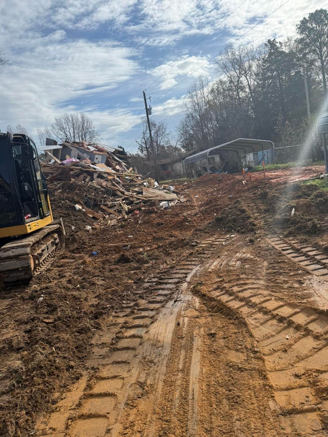 Construction site: pile of rubble, dirt path, excavator, partly cloudy sky.