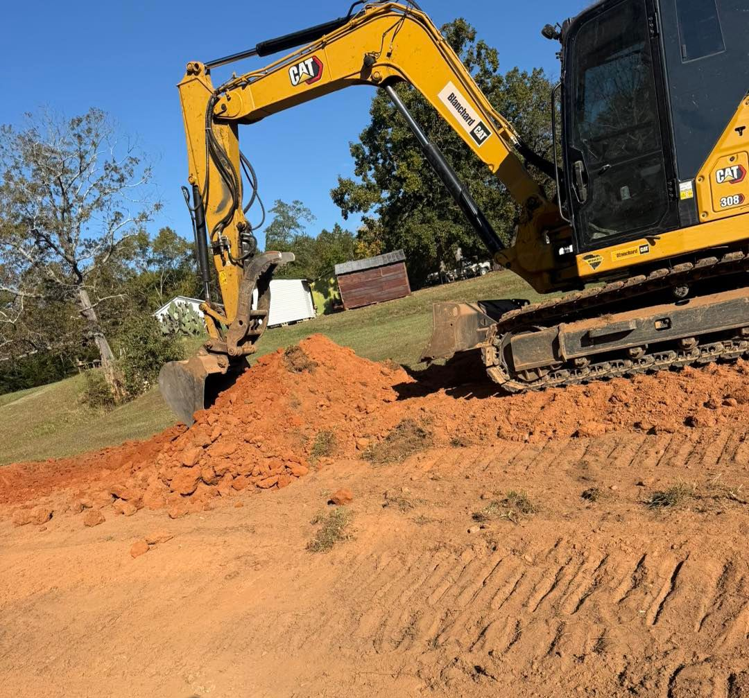 Yellow excavator digging in red dirt on a sunny day.