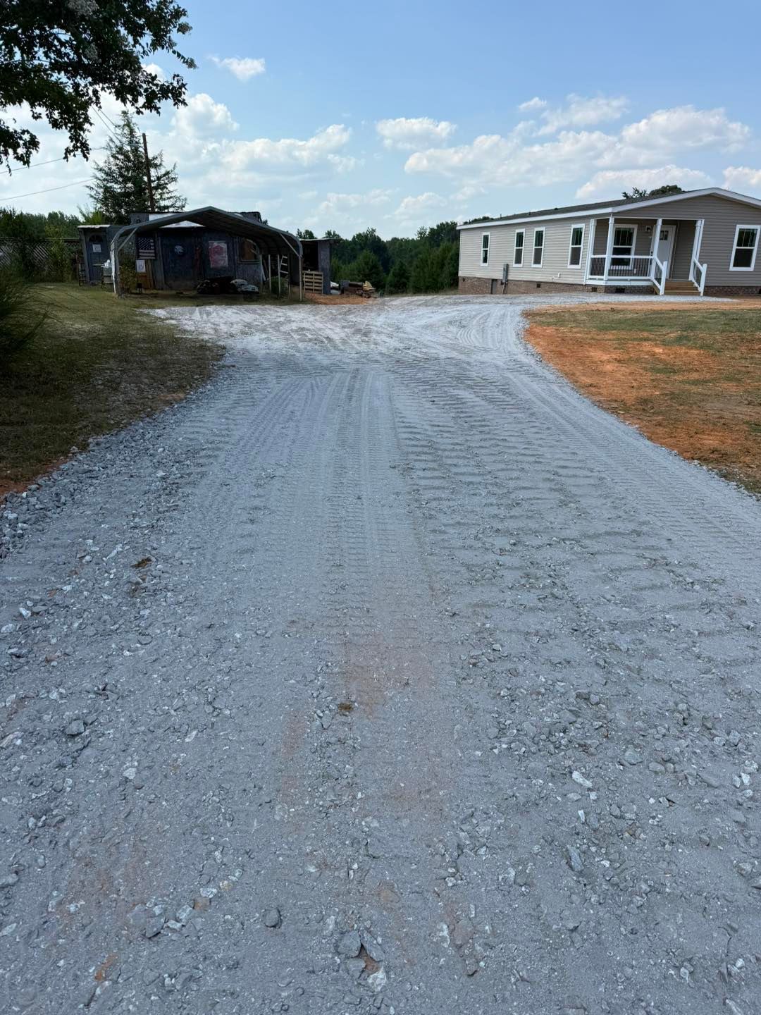 Gravel driveway leading to a mobile home and shed on a sunny day.