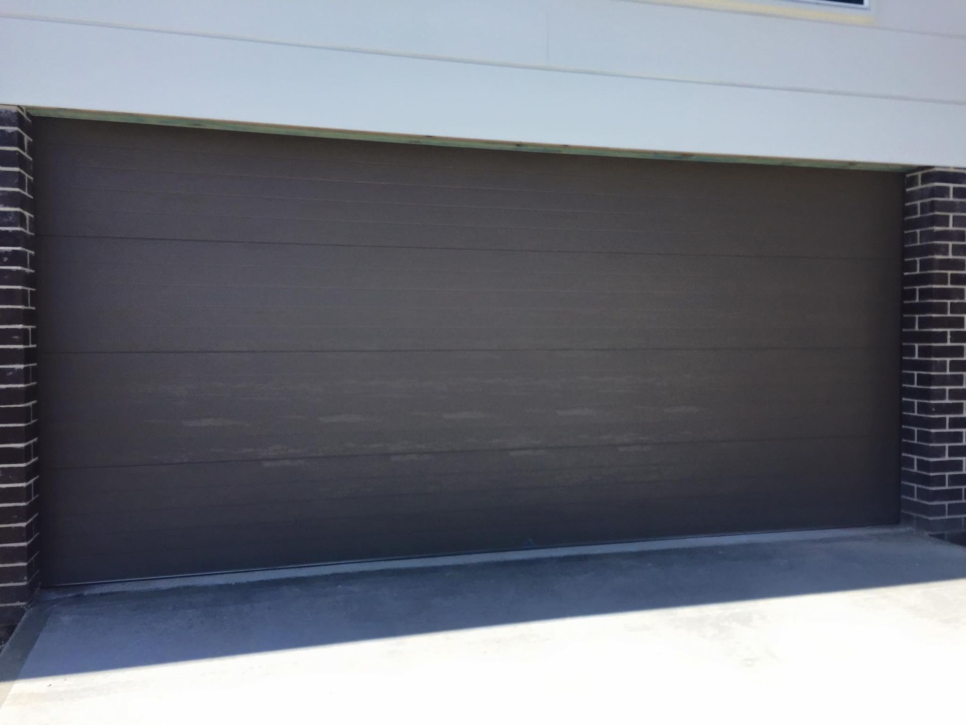 A brown garage door is sitting next to a brick wall. — P & D Garage Doors in Wauchope, NSW