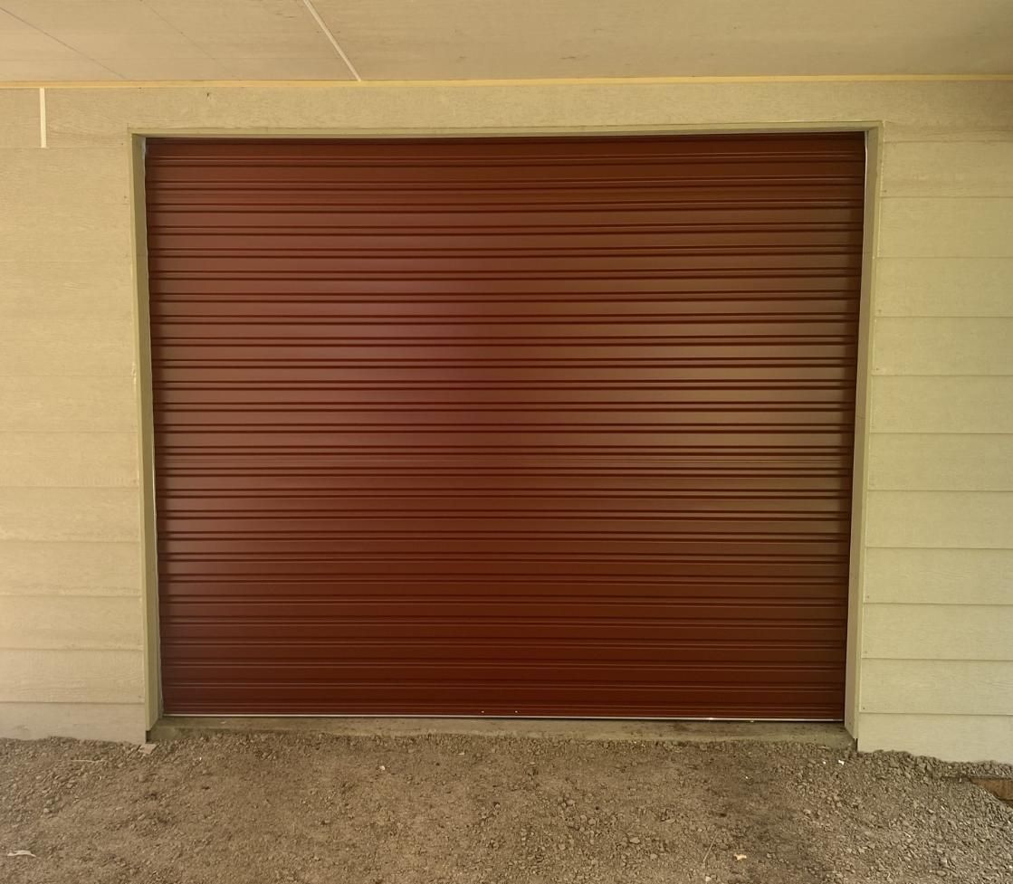 A red garage door is sitting on top of a gravel driveway. — P & D Garage Doors in Taree, NSW