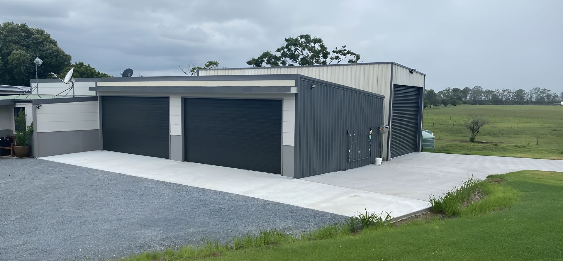 Modern grey metal garage on gravel driveway beside open green fields, showcasing Garage Doors Taree