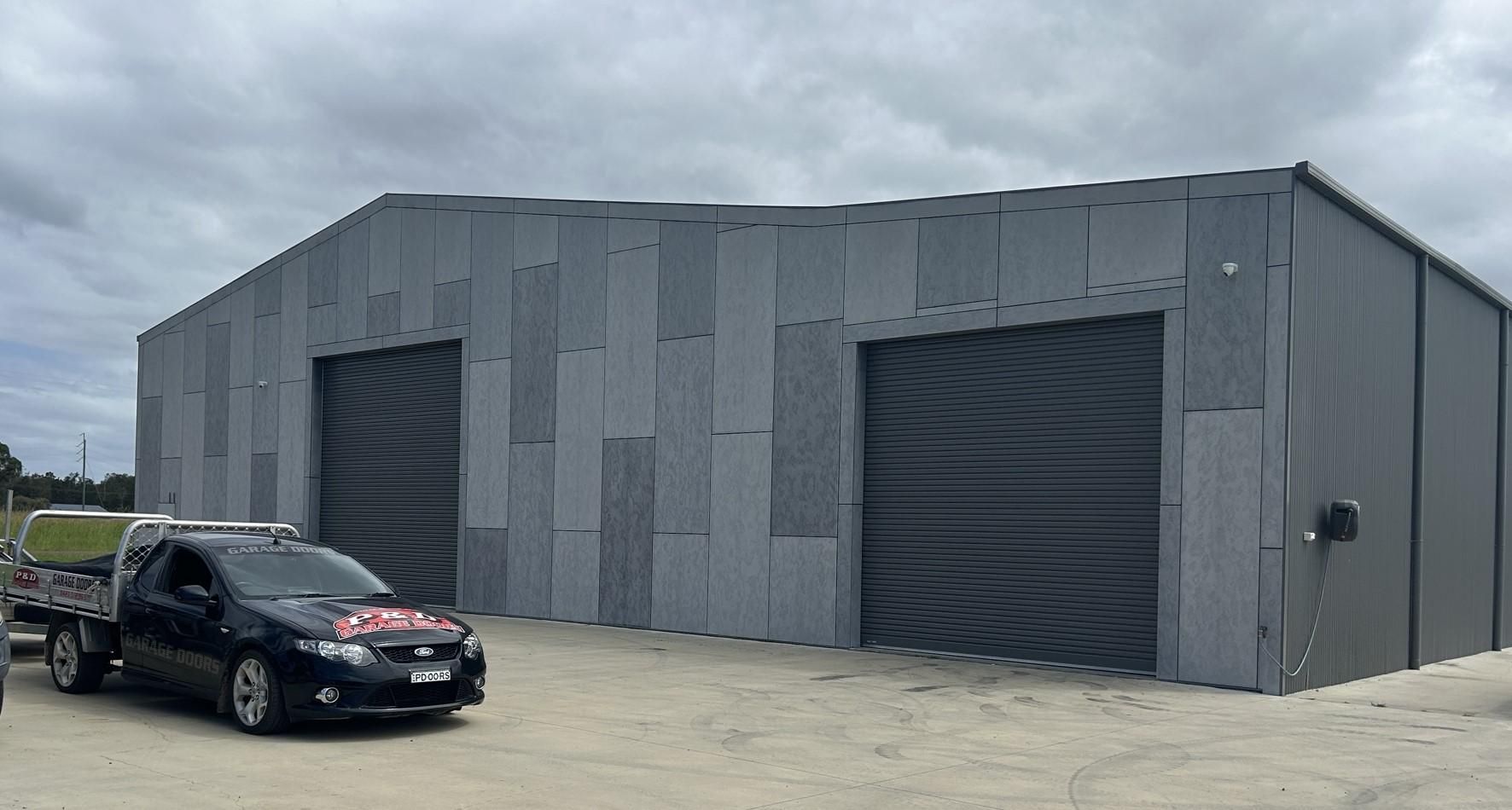 A Black Van is Parked in Front of a Large Building — P & D Garage Doors in Taree, NSW