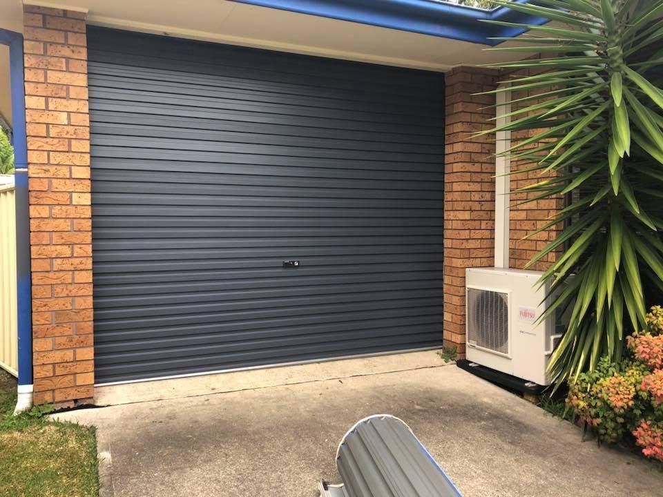 A Blue Garage Door is Sitting Next to a Brick Building — P & D Garage Doors in Wingham, NSW