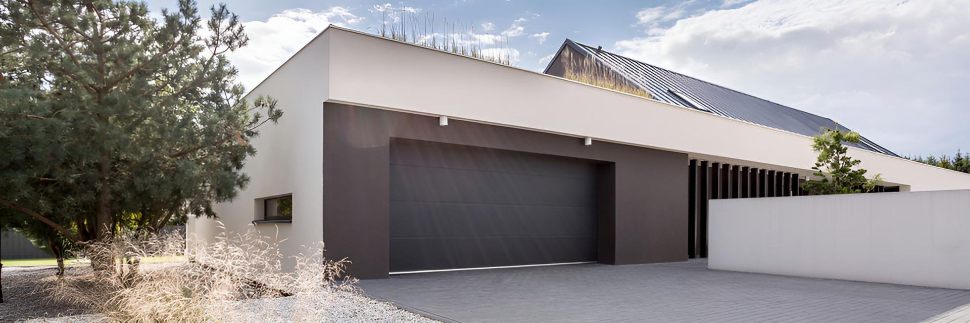A Modern House With a Large Garage Door and Trees in Front of It — P & D Garage Doors in Forster, NSW